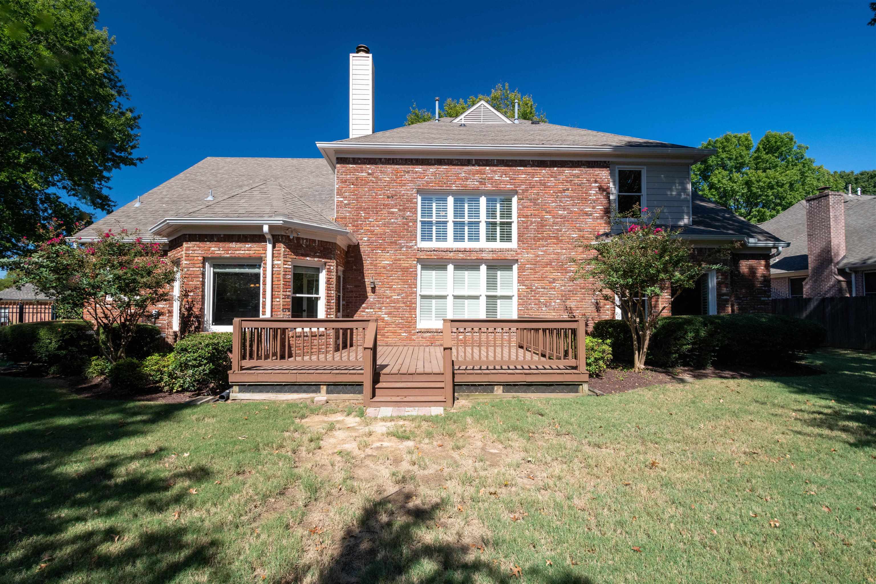 Rear view of a two-story brick house with a raised wooden deck and lawn.