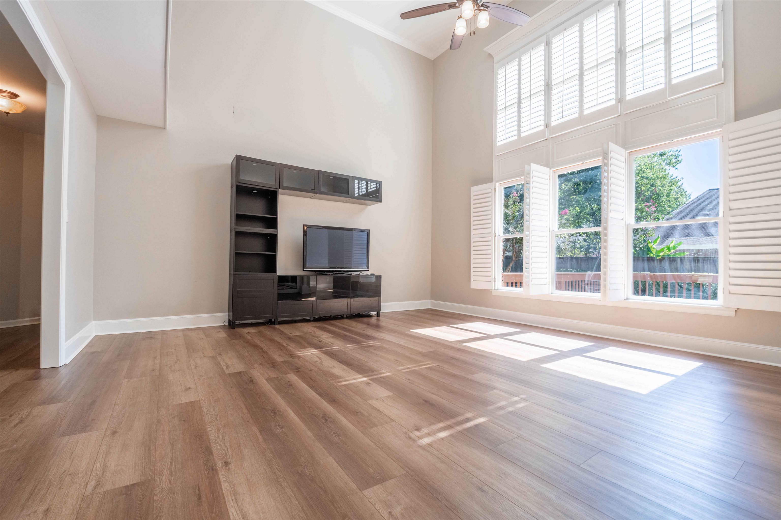 Bright living room with tall shuttered windows, wood flooring, and a dark built-in media unit.