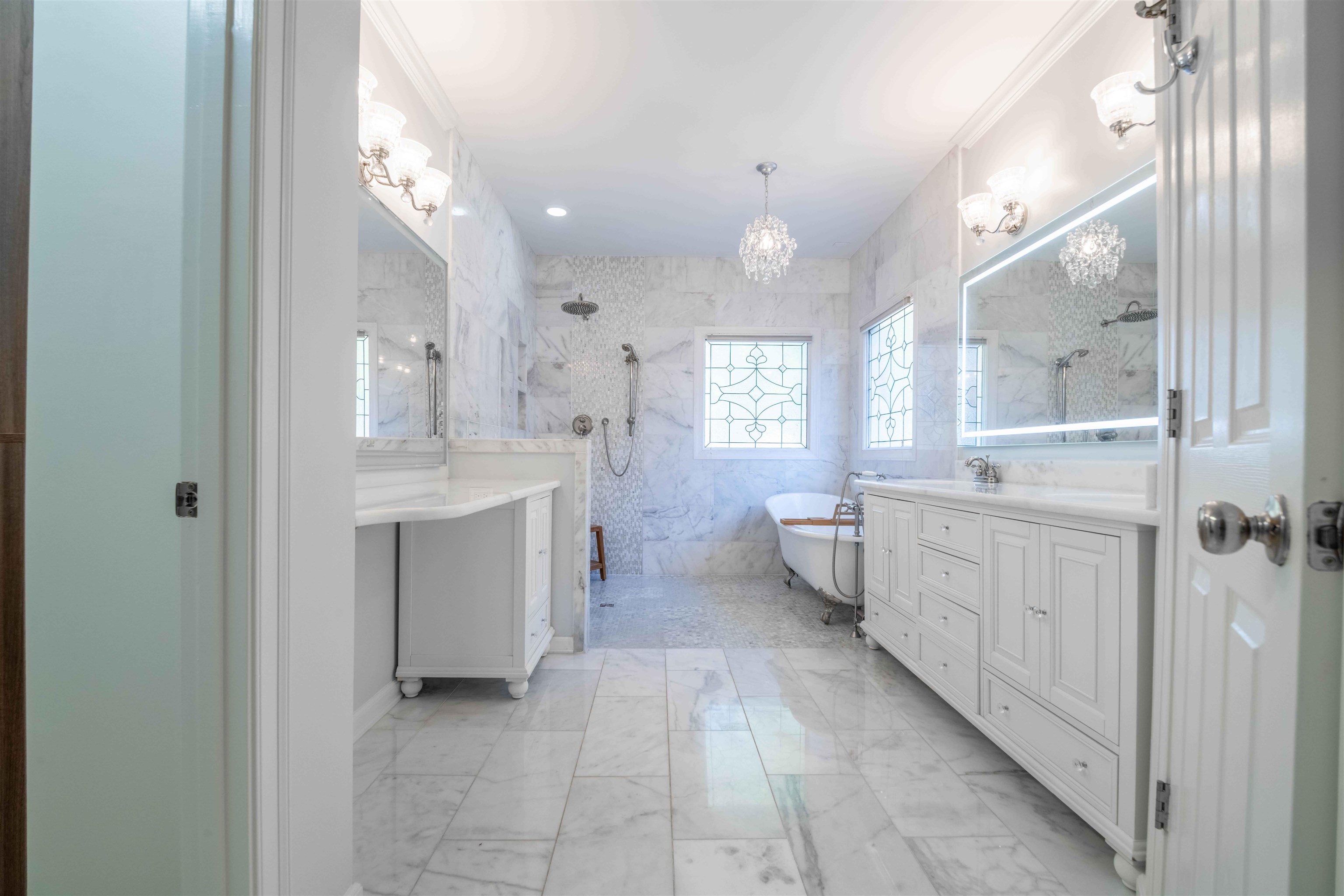 Marble-tiled bathroom with a freestanding tub, double vanity, and chandelier.