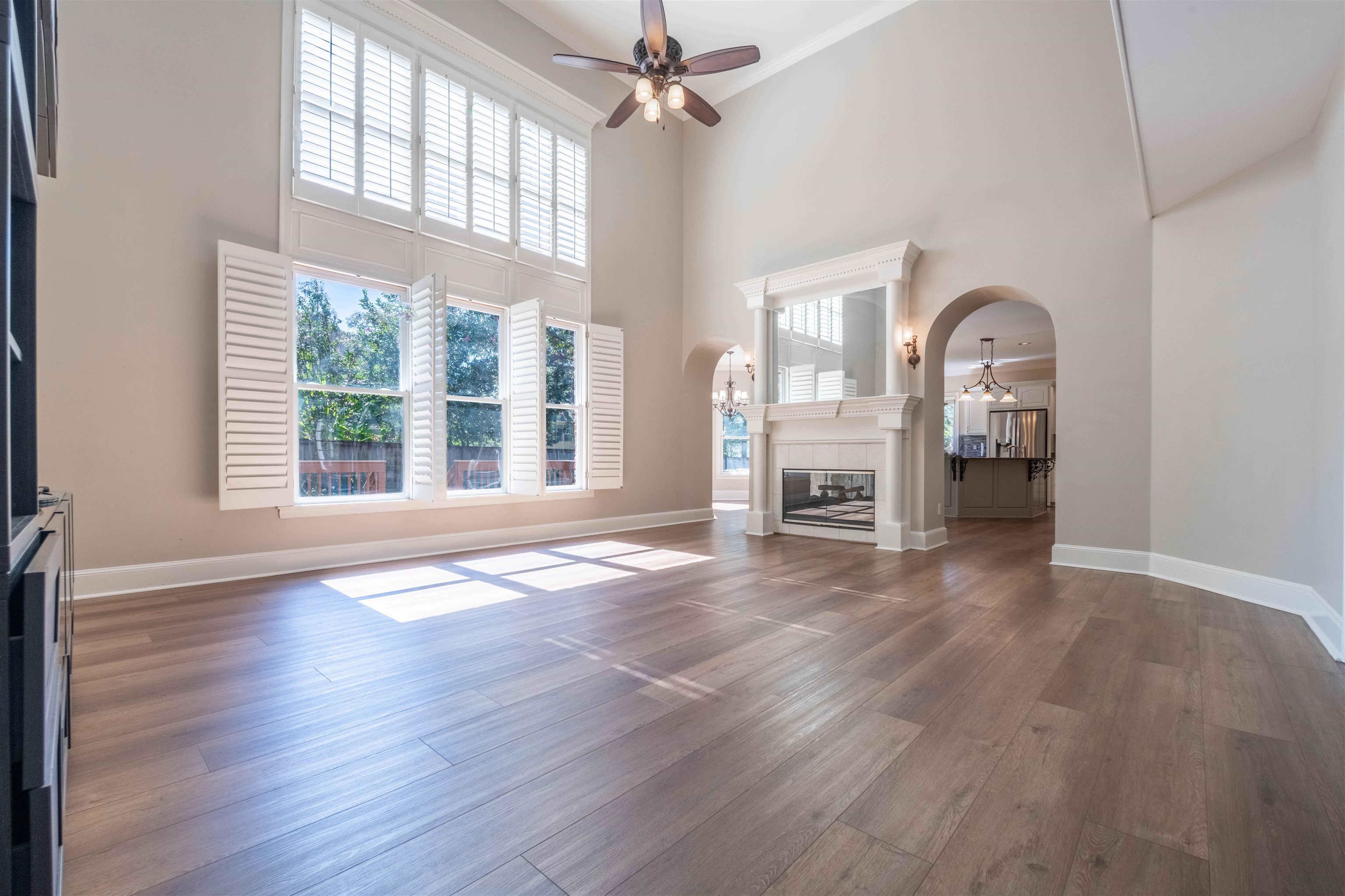 Two-story living room with tall shuttered windows, hardwood floors, and a white fireplace.
