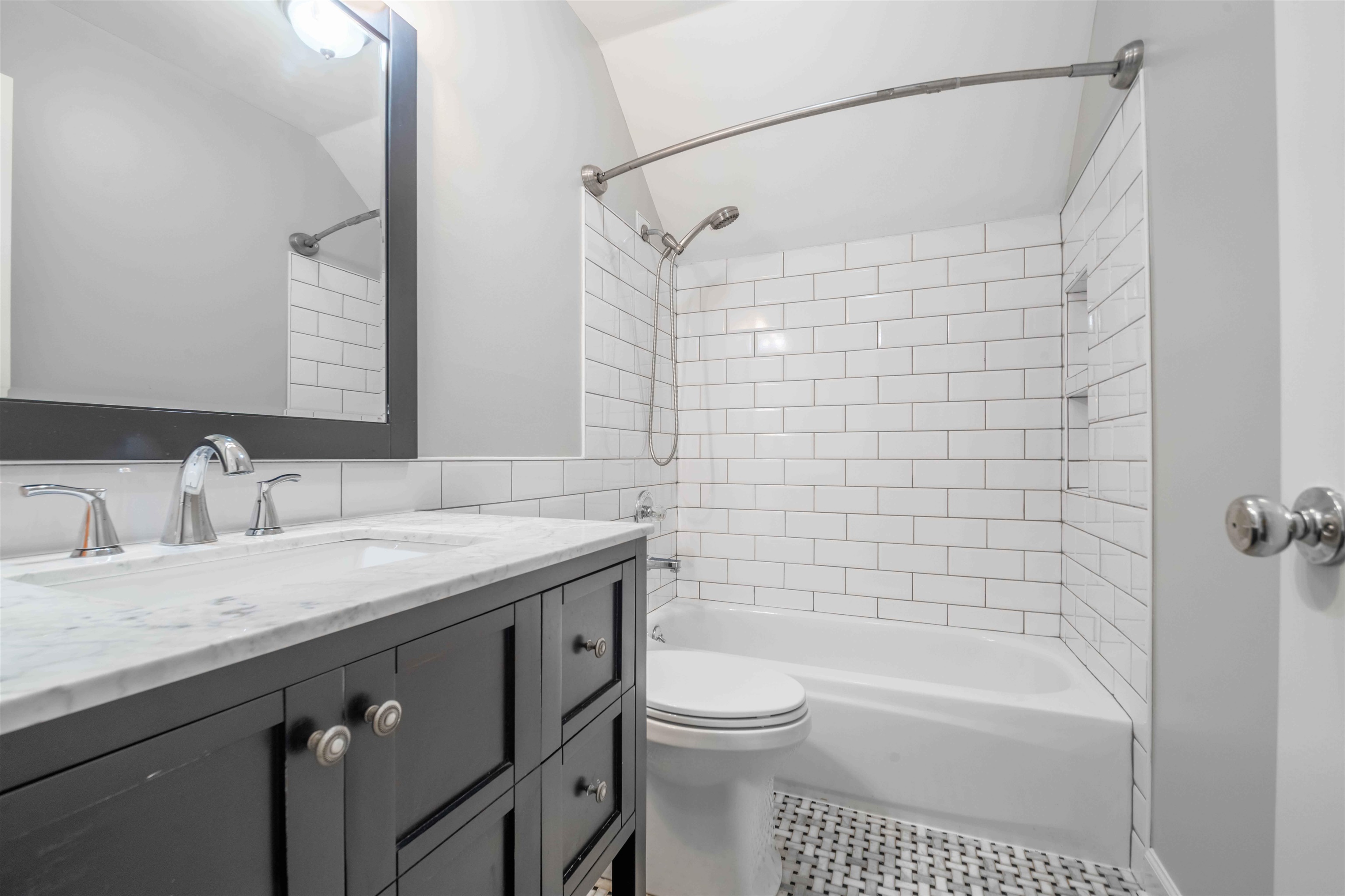 Bathroom with a dark vanity, white subway-tile tub surround, and mosaic tile floor.