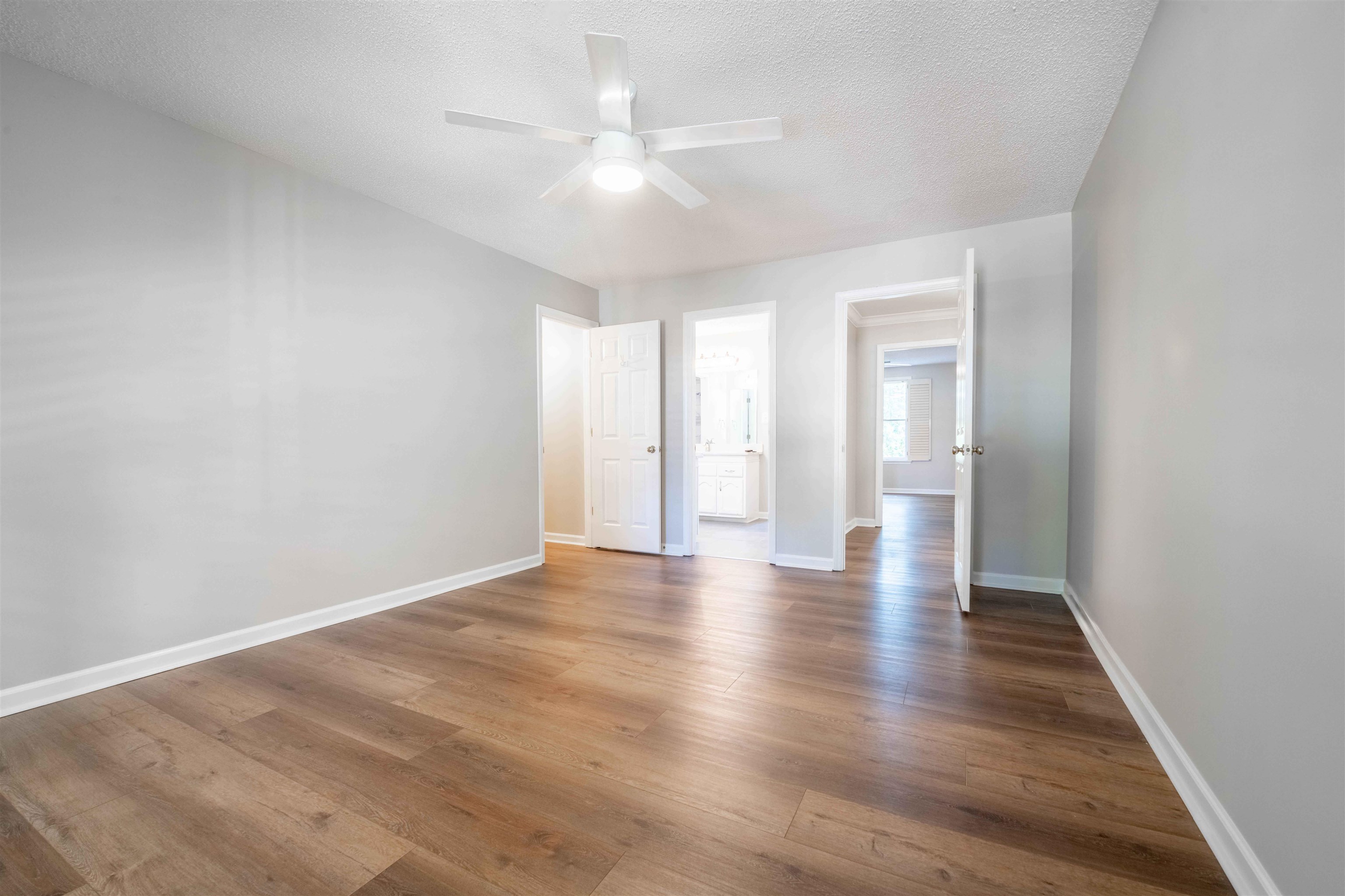 Empty room with wood-look flooring, gray walls, and a ceiling fan.