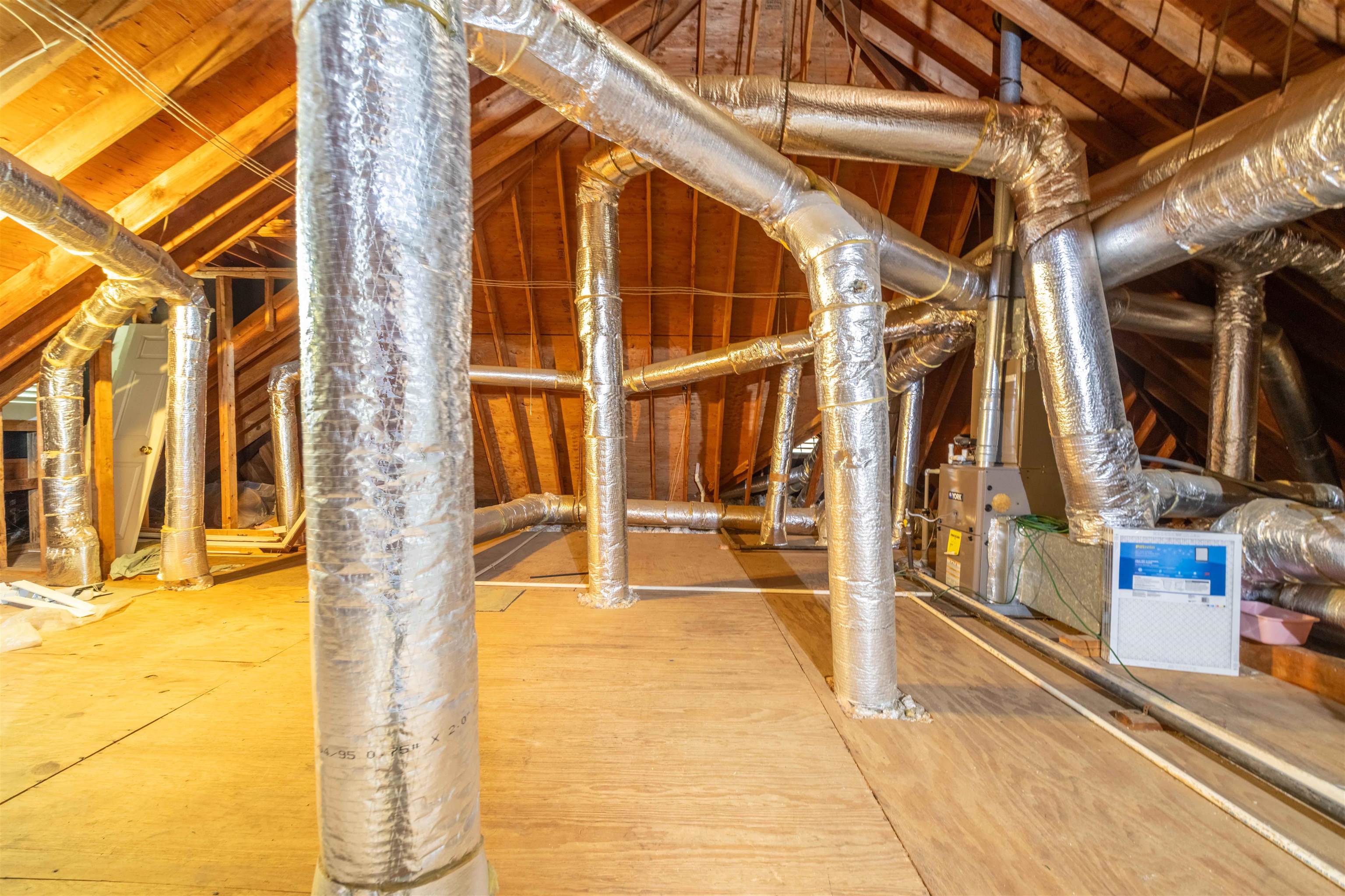 Unfinished attic with exposed wooden rafters, extensive silver HVAC ductwork, and a furnace.
