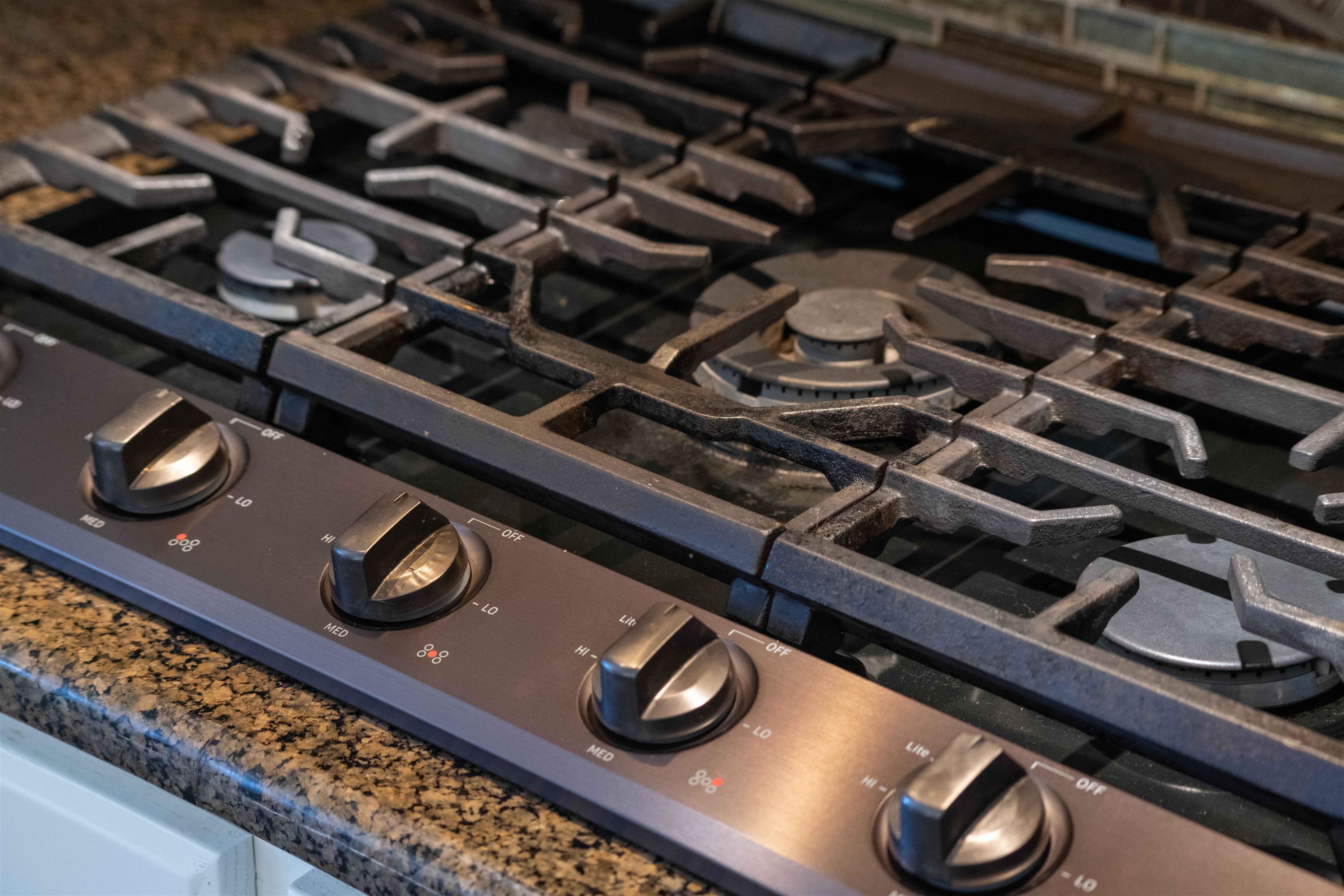 Kitchen gas cooktop with heavy cast-iron grates and metal control knobs on a granite counter.