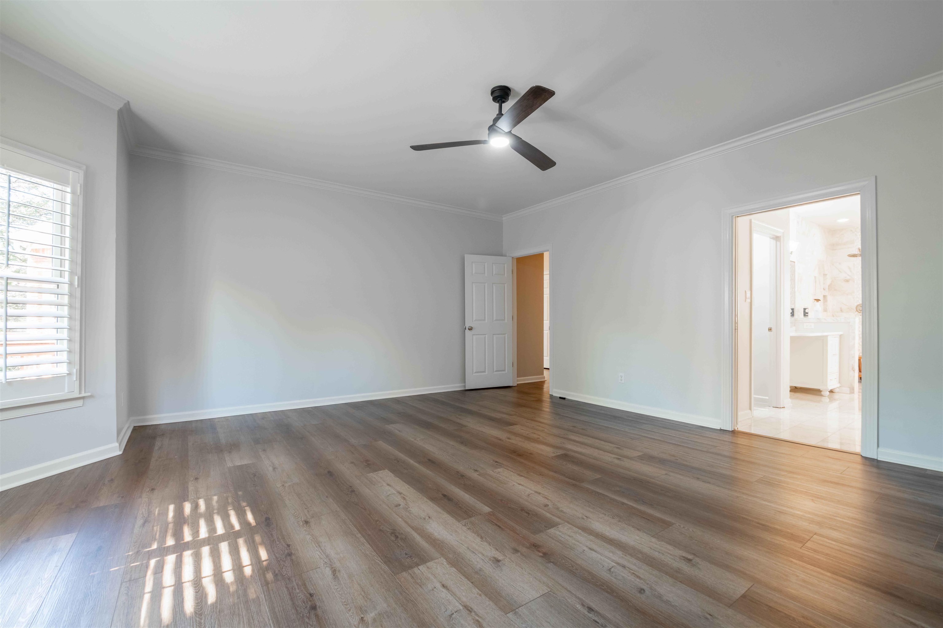 Vacant bedroom with wood-look flooring, a ceiling fan, and plantation-shuttered window.