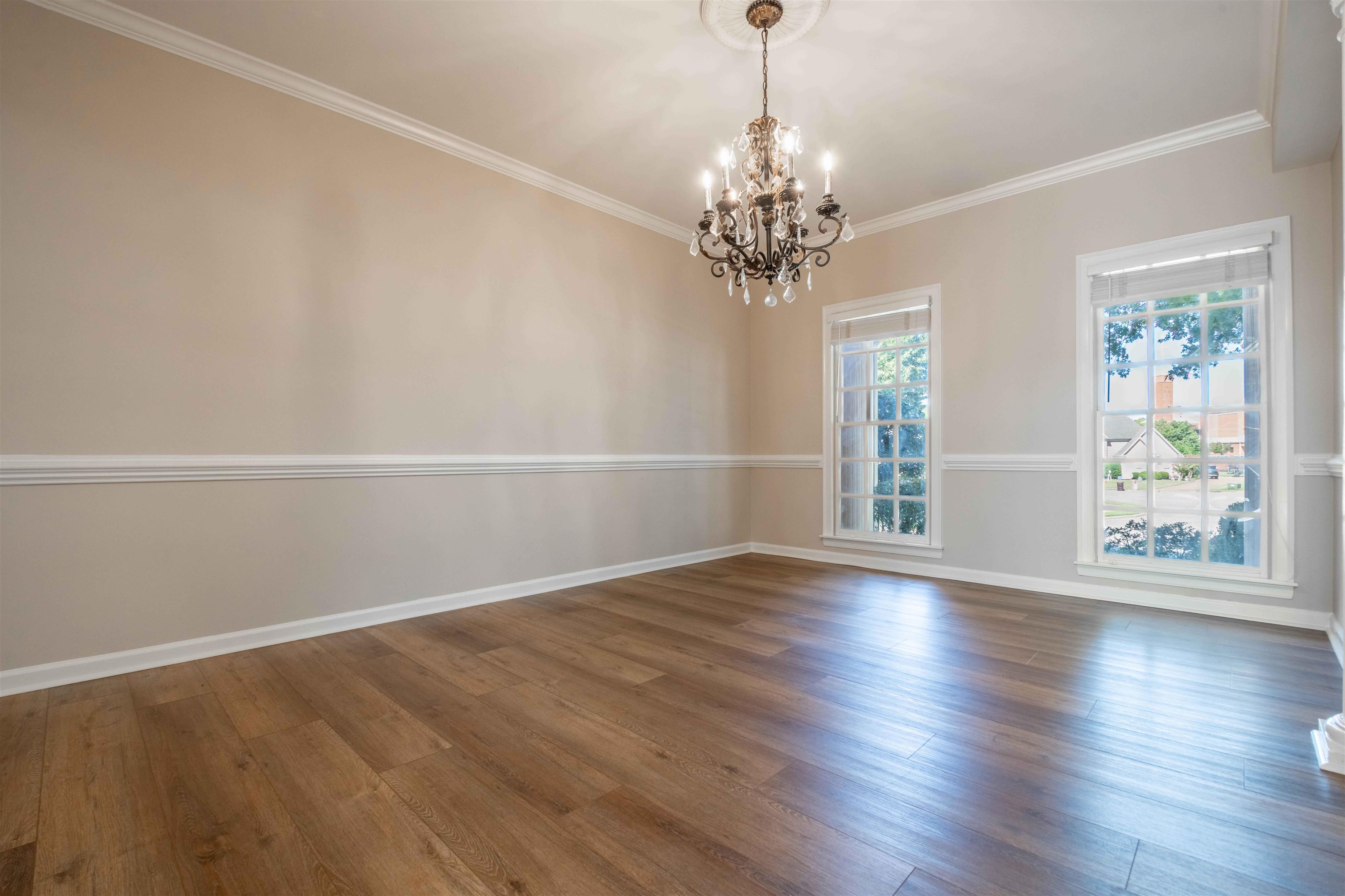 Empty dining room with a crystal chandelier, wood flooring, and two tall windows.