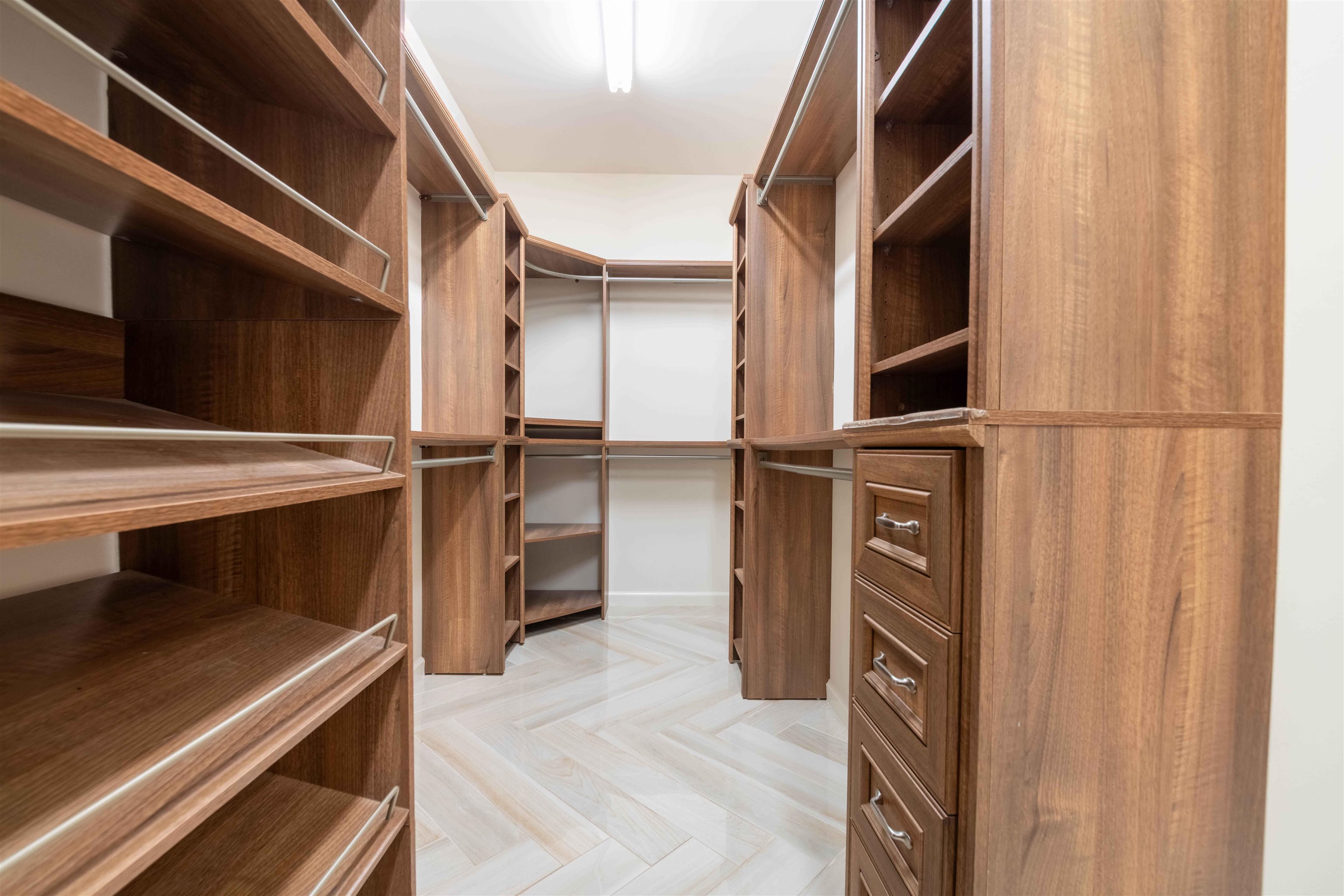 Walk-in closet with extensive walnut shelving, hanging rods, drawers, and light tile flooring.