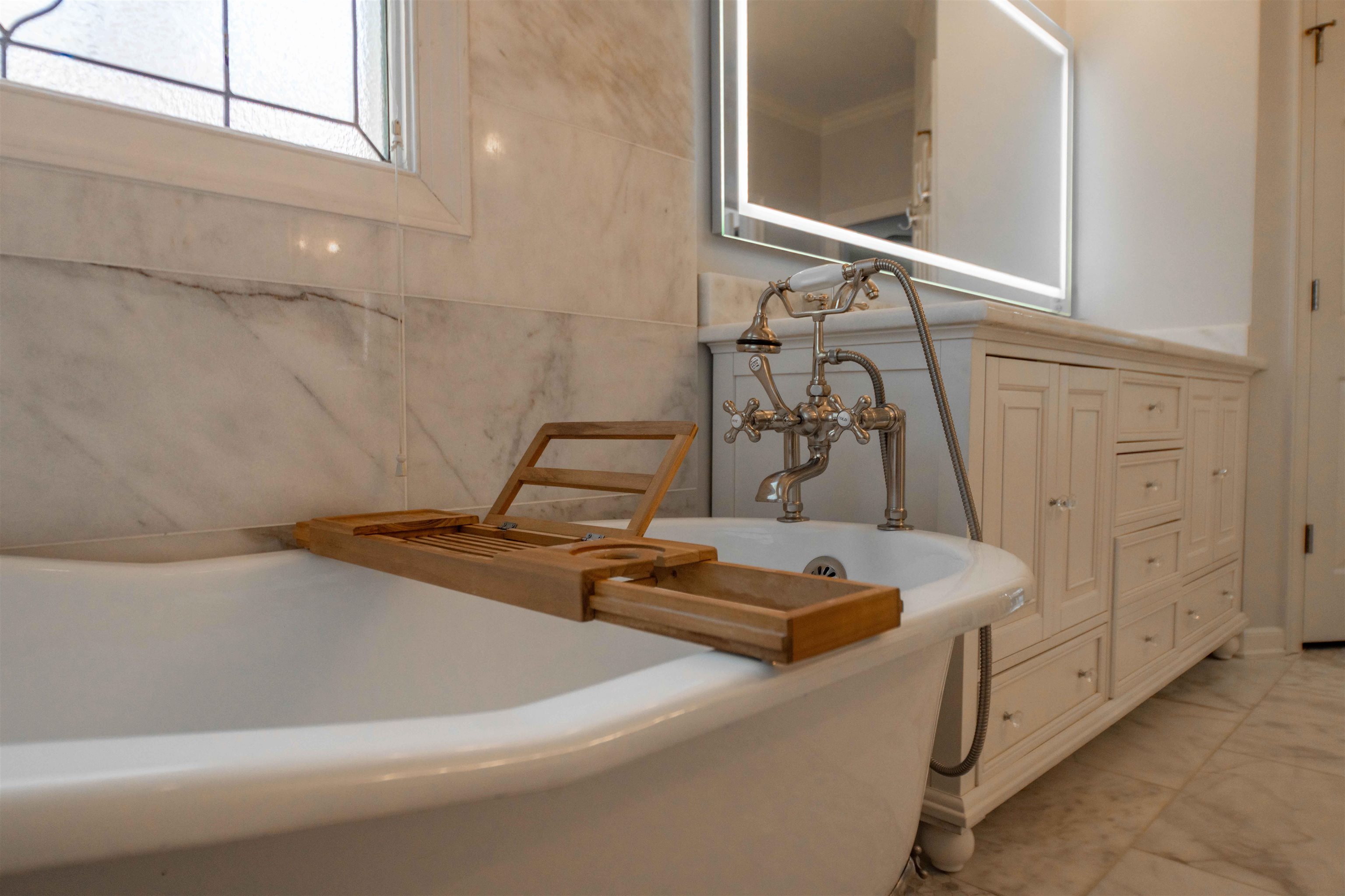 Freestanding bathtub with a wooden bath tray, brass fixtures, and marble tile.