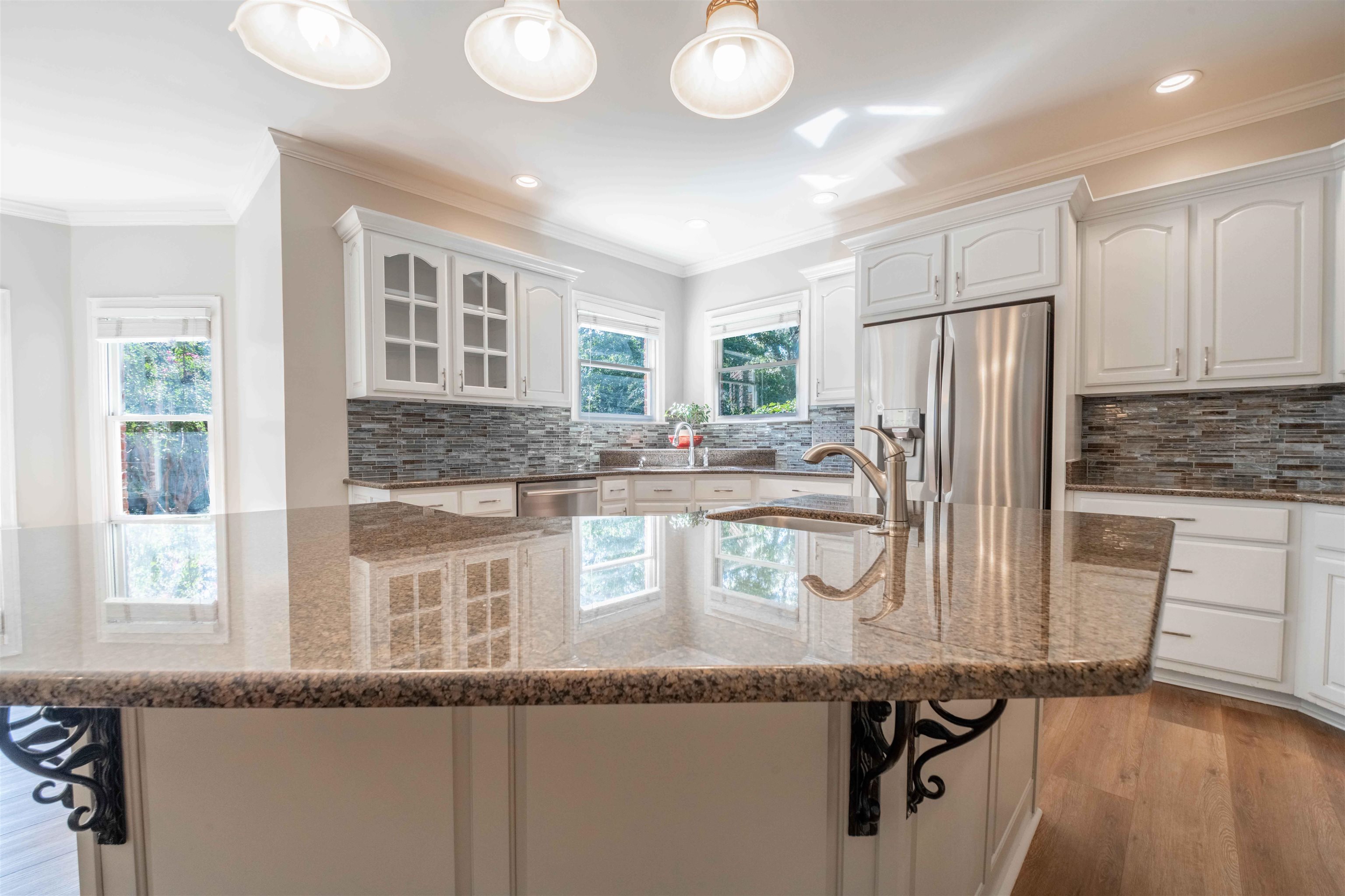 Bright kitchen with white cabinets, a large granite island, stainless refrigerator, and tiled backsplash.