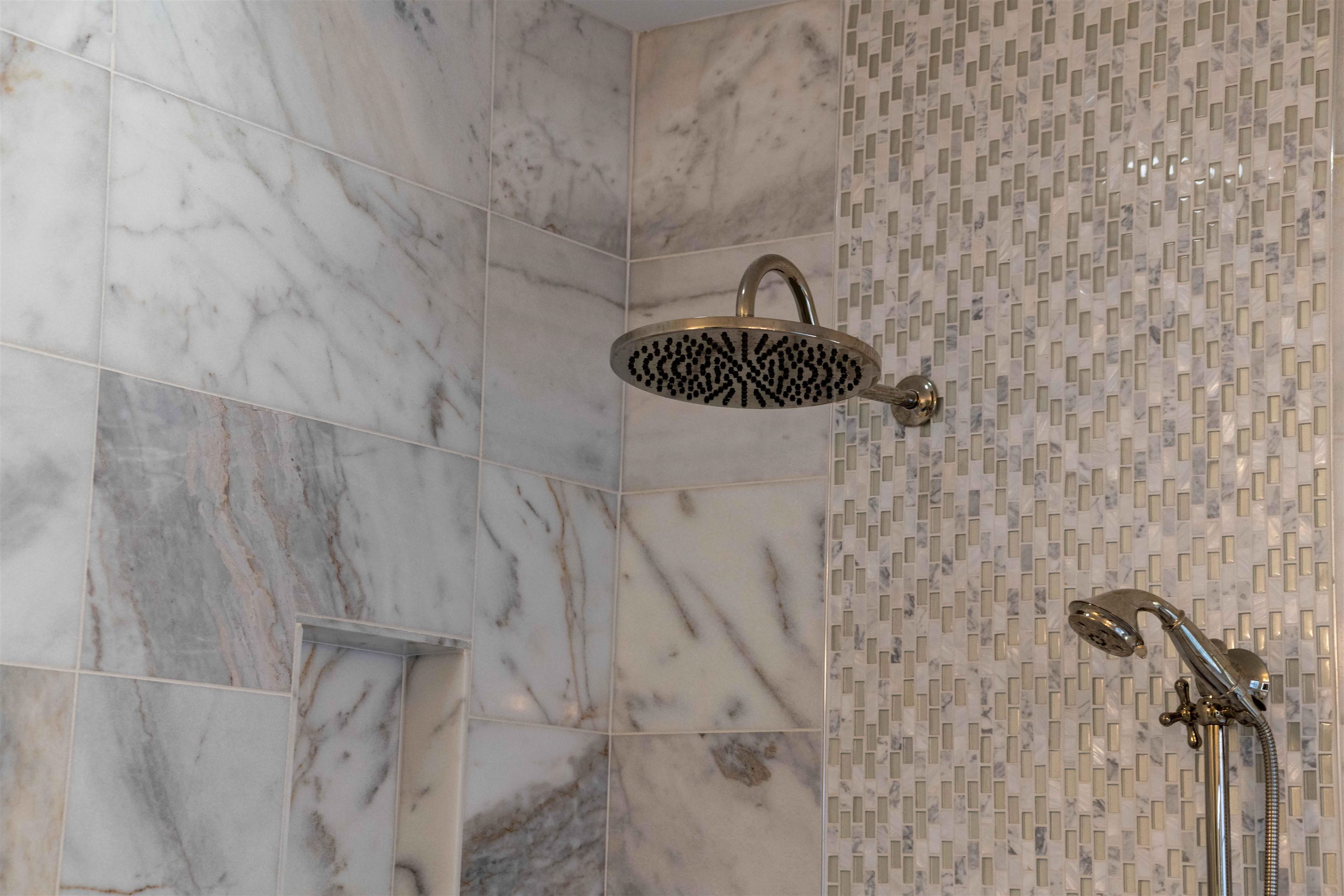 Marble-tiled shower with a large overhead rain showerhead and handheld sprayer.