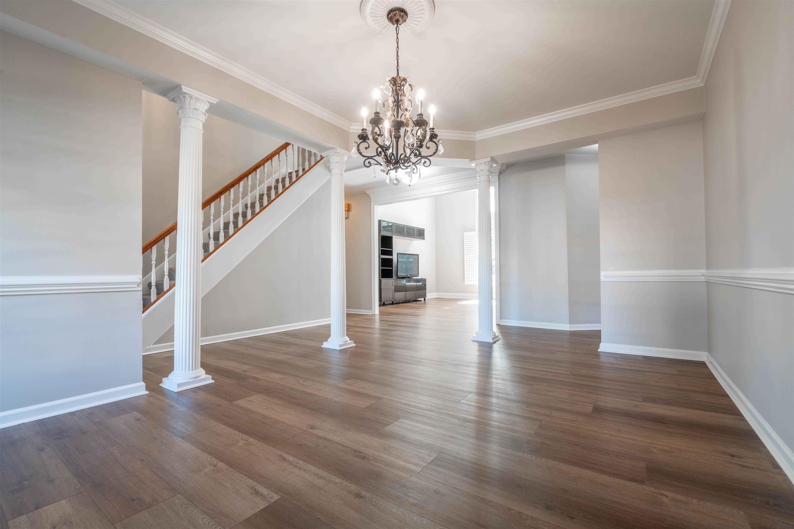 Open foyer with wood floors, a staircase, white columns, and a chandelier.
