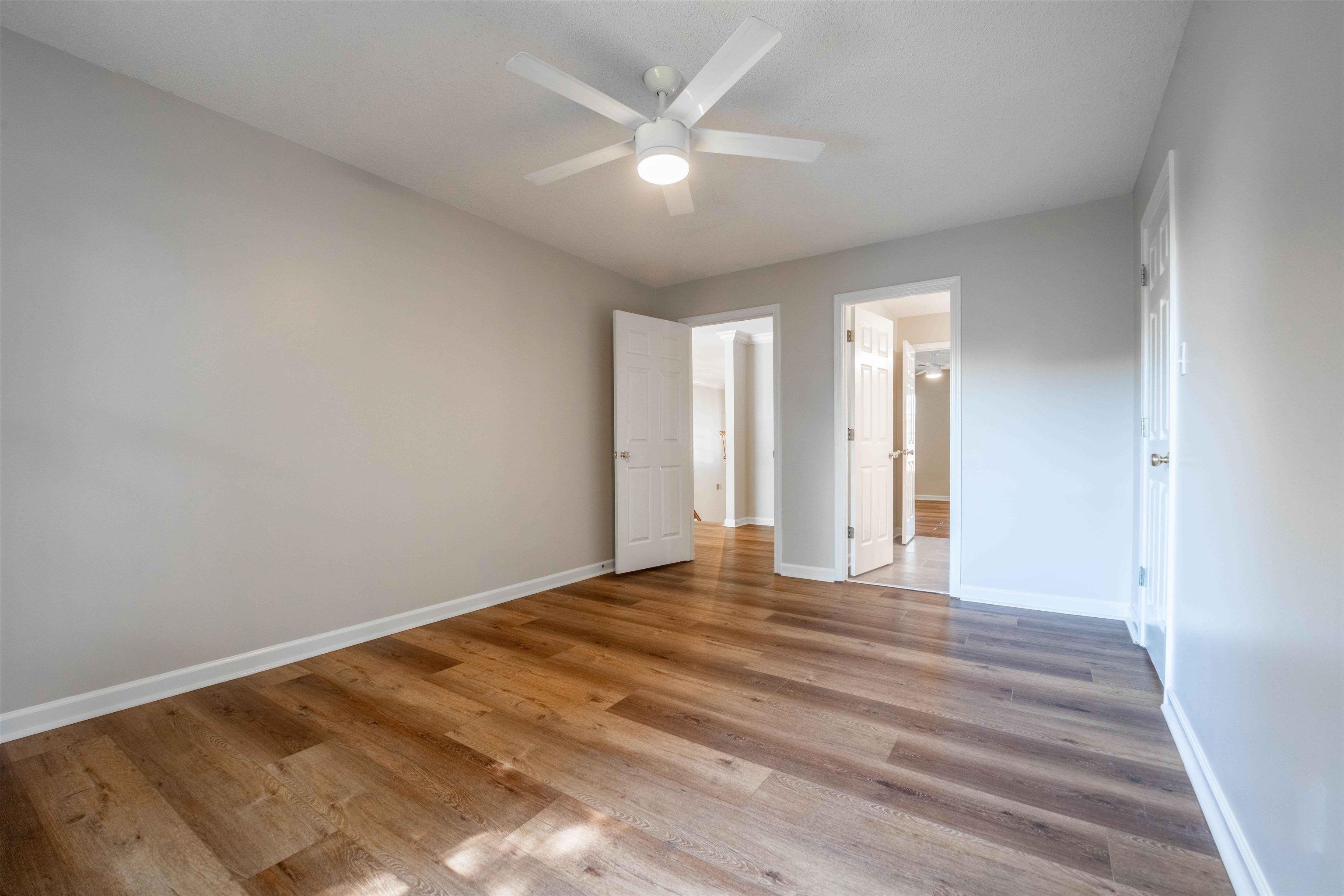 Vacant room with wood flooring, gray walls, a ceiling fan, and multiple open doorways.