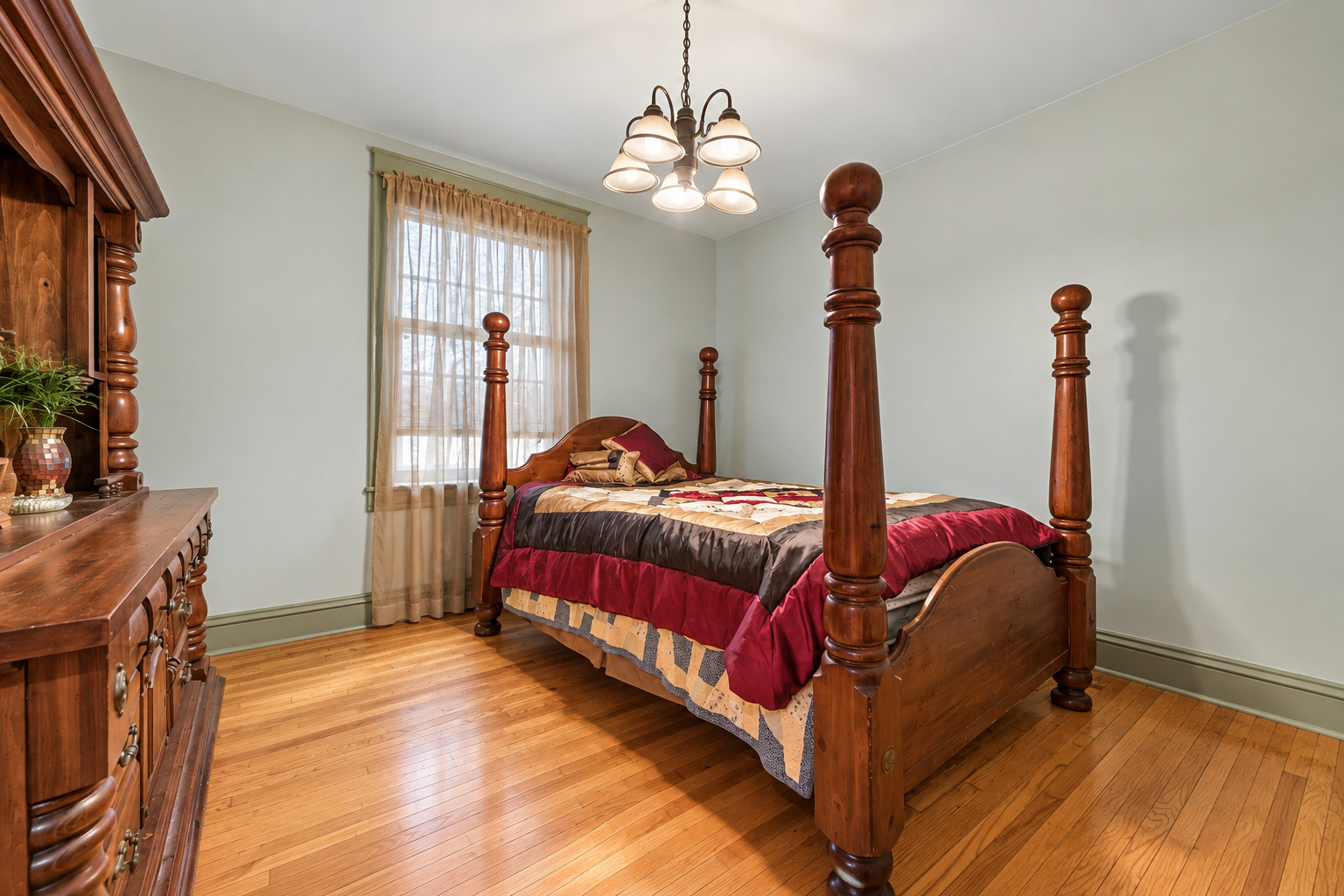 Bedroom with a dark wood four-poster bed, burgundy bedding, and hardwood floors.