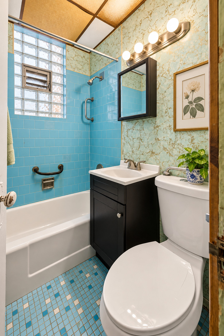 Bathroom with bright blue tile, glass-block window, black vanity, and white bathtub.