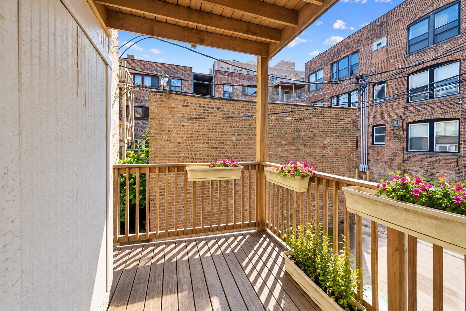 Covered wooden balcony with flower boxes overlooking neighboring brick apartment buildings.