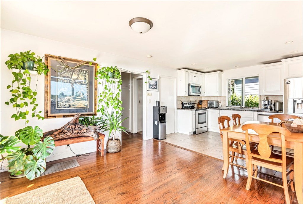 Kitchen and dining area with white cabinets, a wooden table, hardwood floors, and leafy plants.