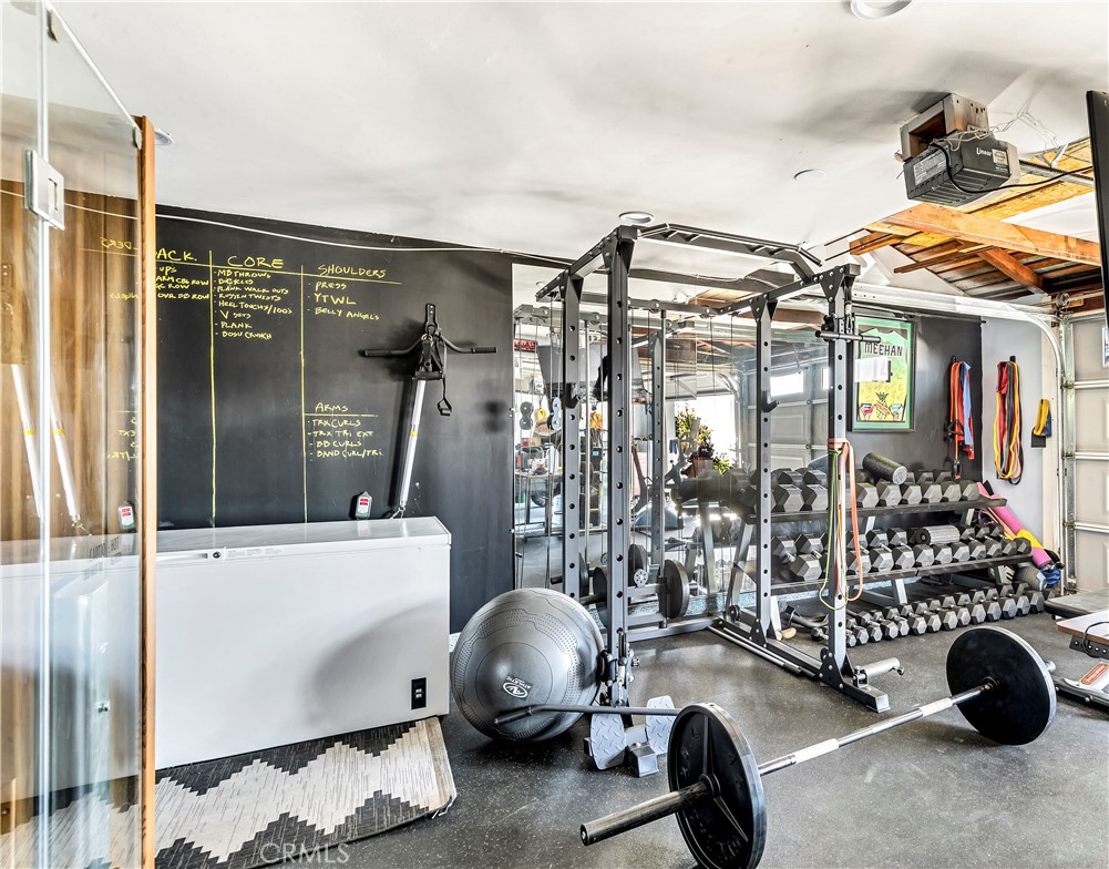 Home gym with a weight rack, rows of dumbbells, and a barbell on the floor.