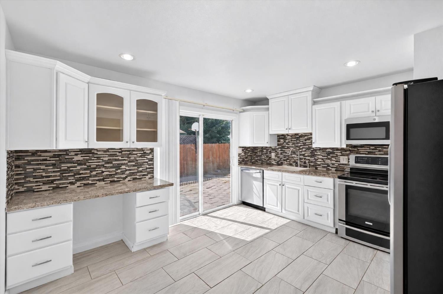 Kitchen with white cabinetry and mosaic backsplash, opening through sliding glass doors to a paved patio.