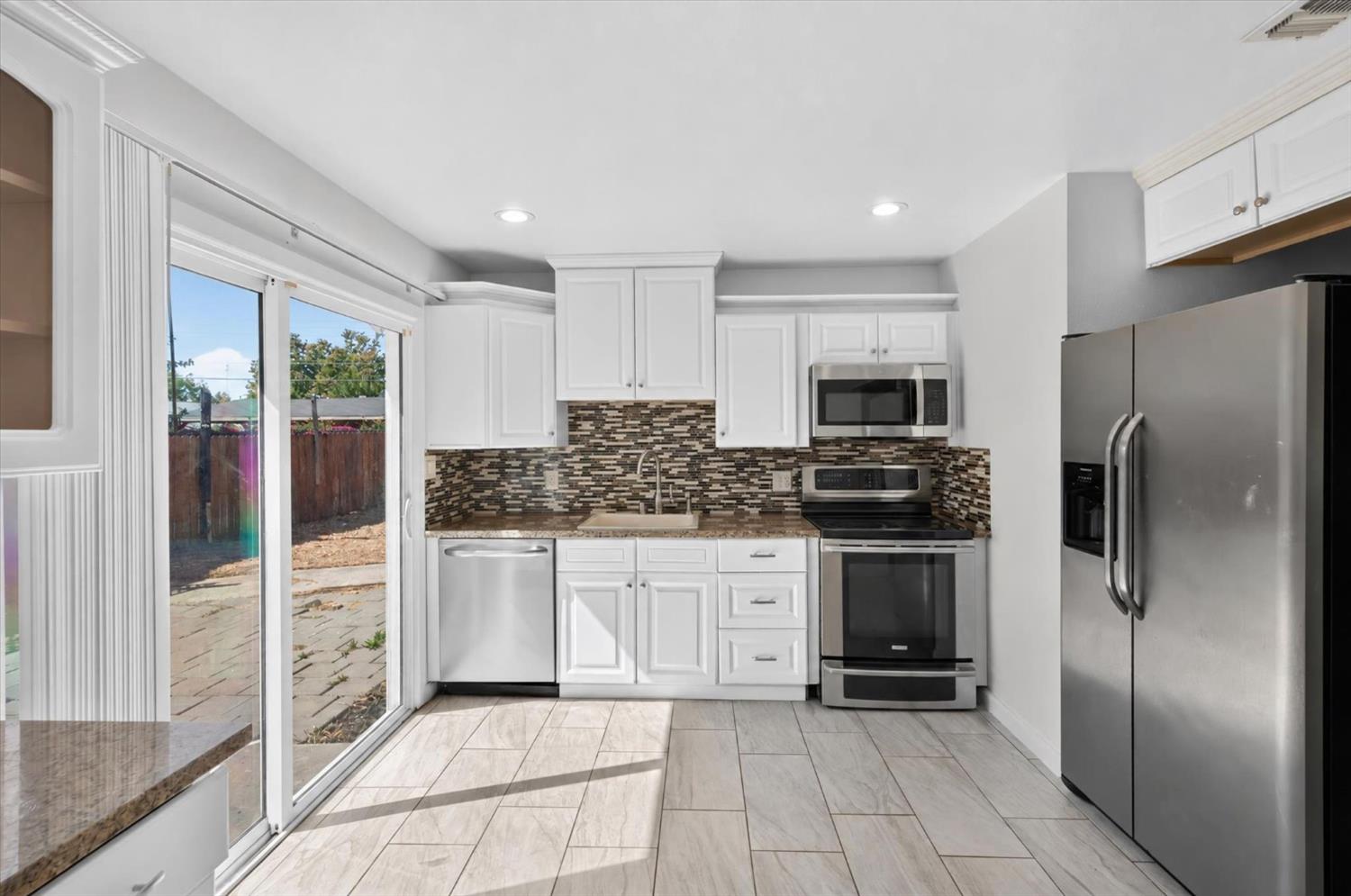 Kitchen with white cabinetry, stainless steel appliances, patterned backsplash, and sliding glass door to the patio.