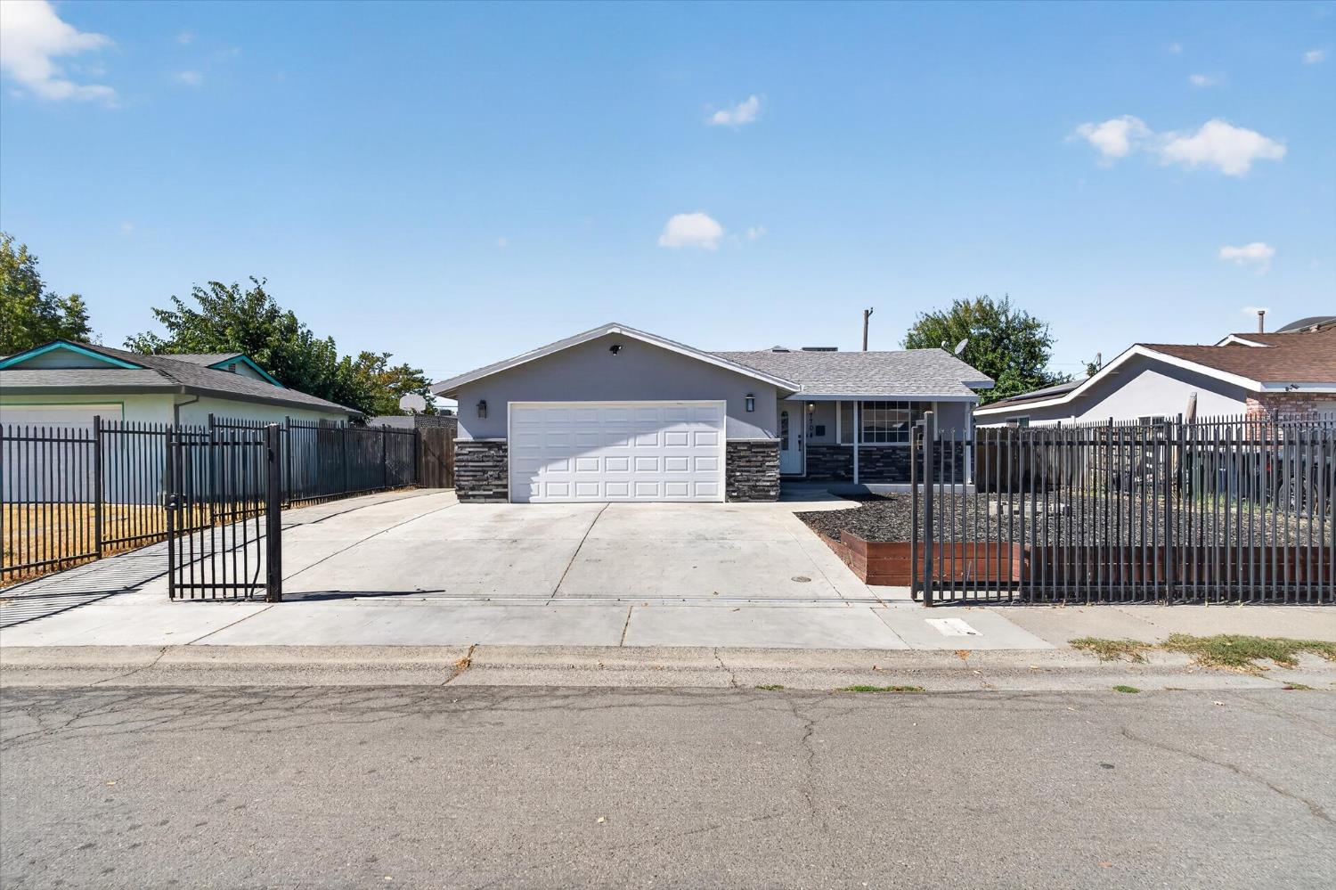 Single-story gray home with stone accents, a double garage, and a fenced concrete driveway.