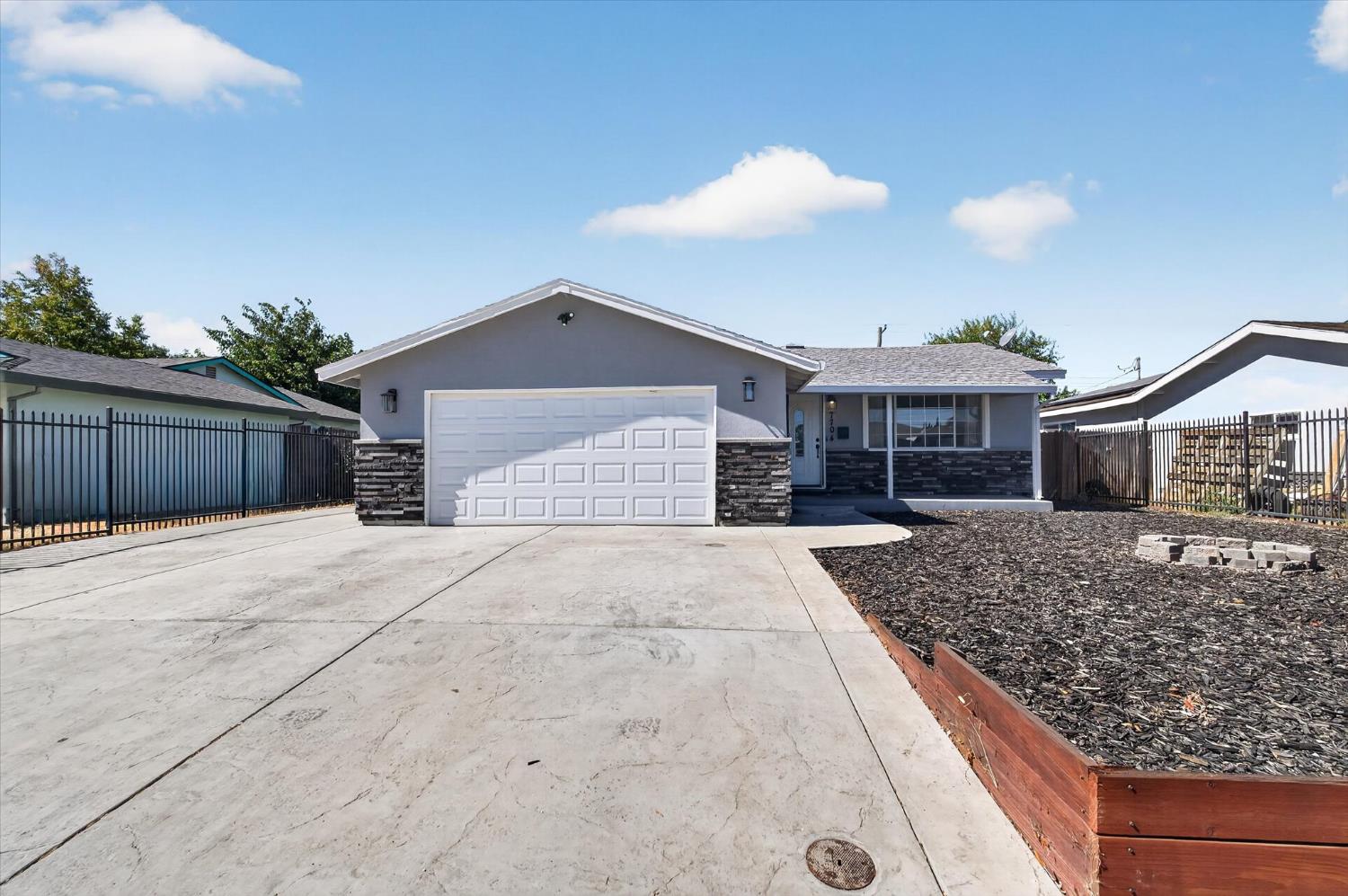 Gray single-story home with a white double garage door, broad driveway, and fenced front yard.