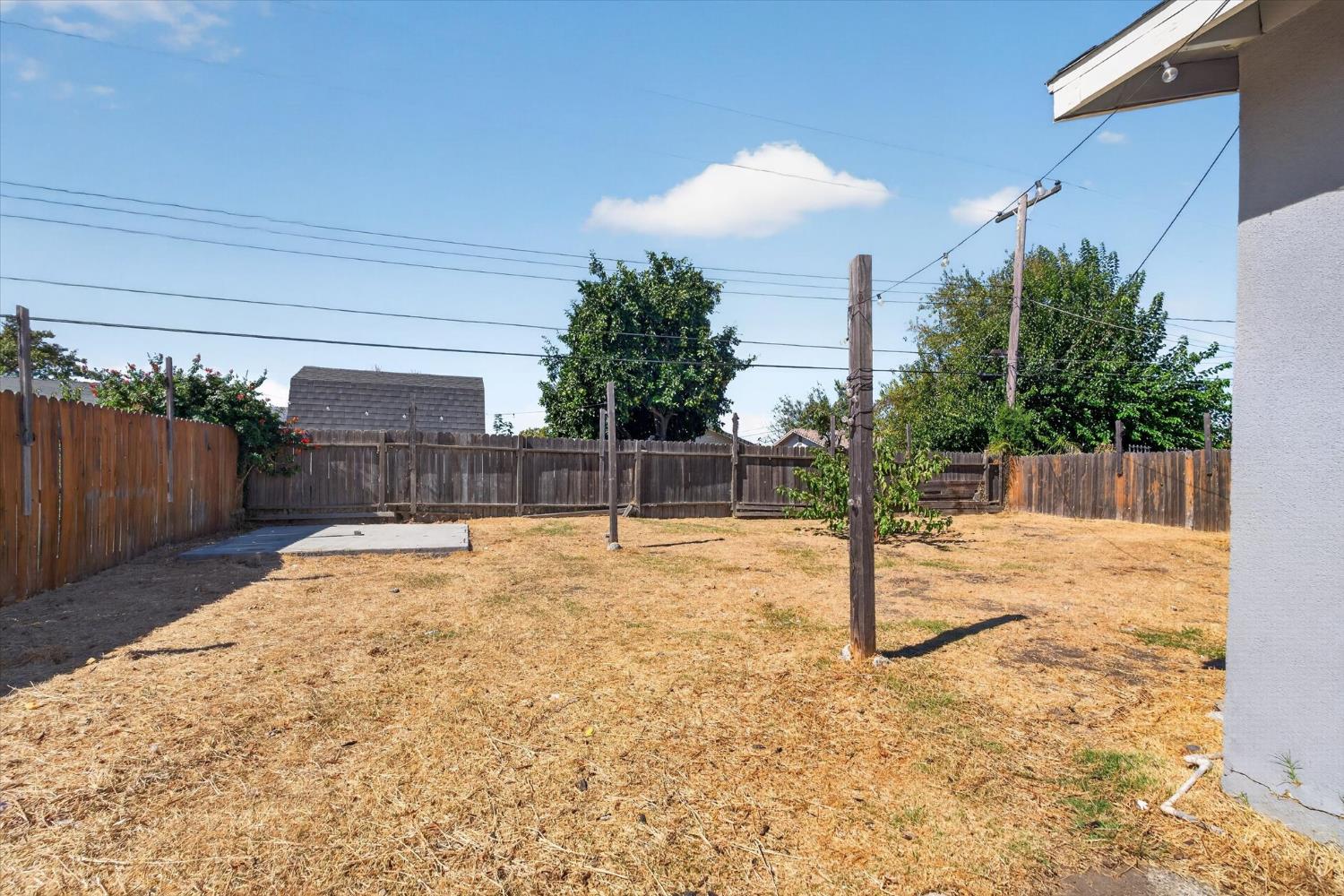 Fenced backyard with dry grass, clothesline poles, and a small concrete pad.