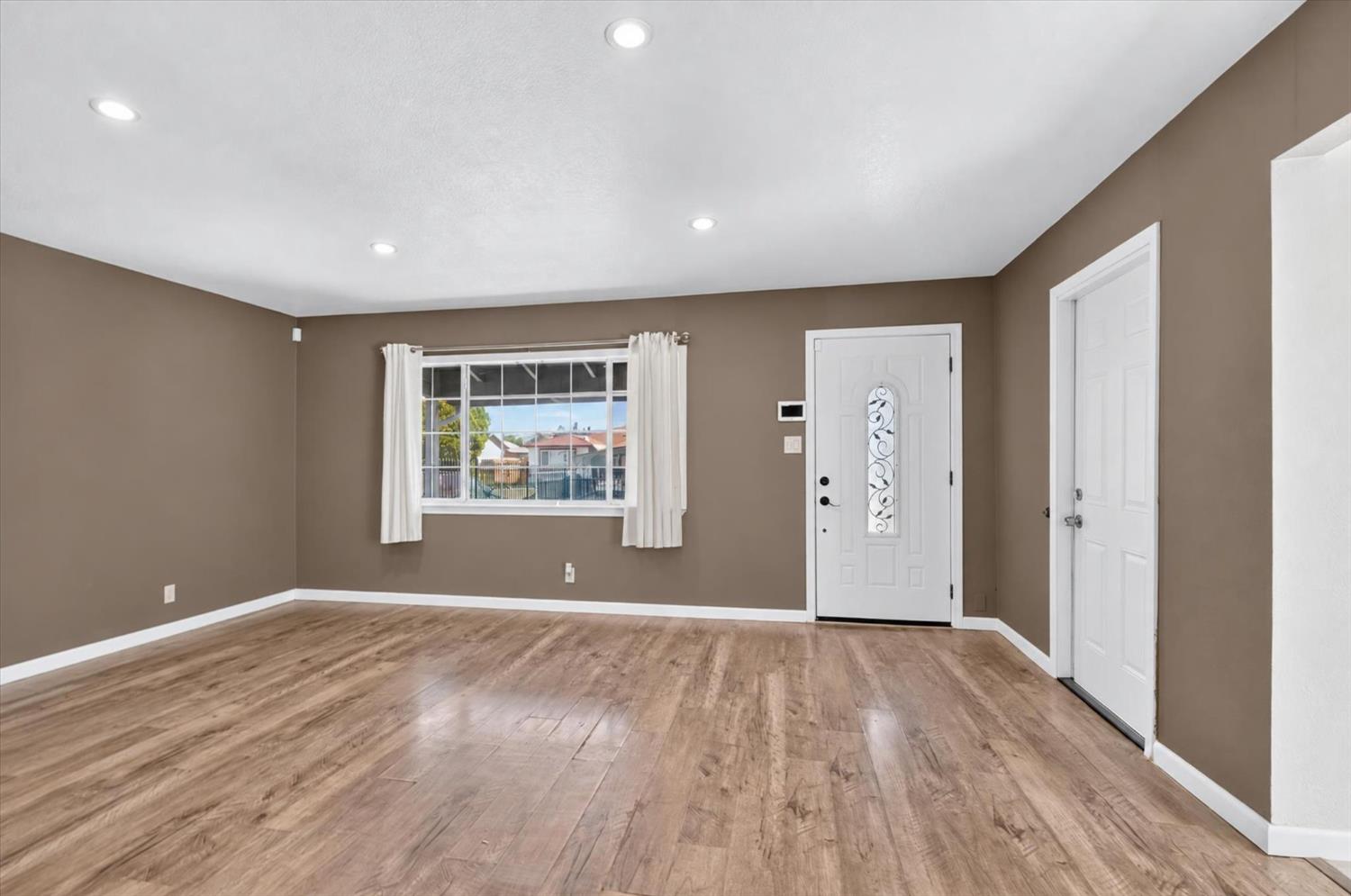 Vacant living room with wood-look flooring, taupe walls, and a white front door with decorative glass.