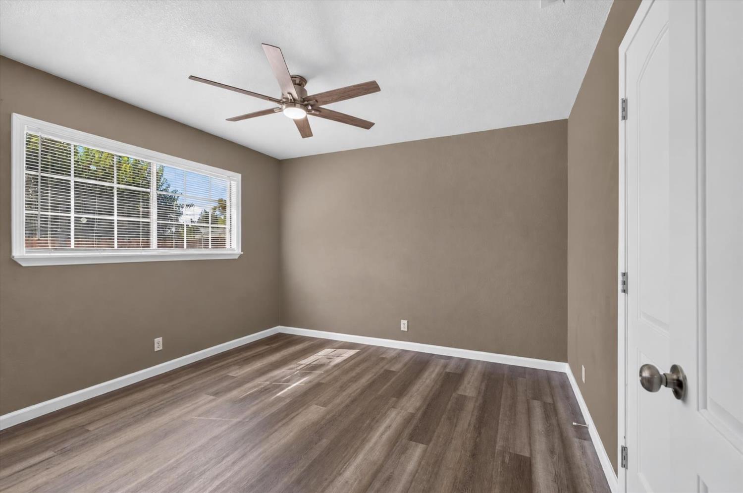Empty room with wood-look flooring, a wide window, and a ceiling fan.