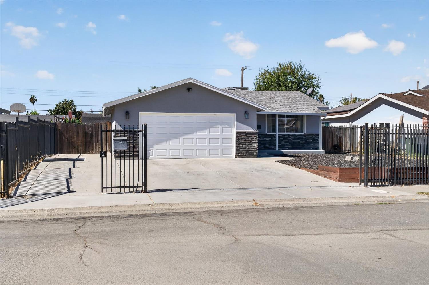 Gray single-story home with a white garage, stone veneer, and gated driveway.