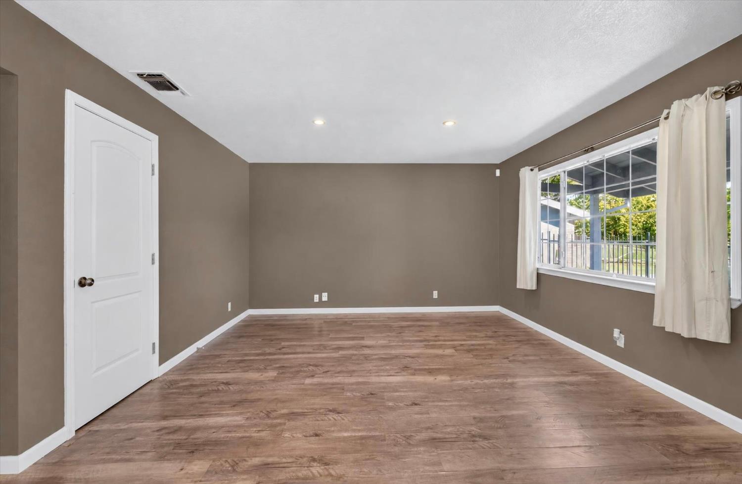 Empty room with brown walls, wood-look flooring, and a large curtained window.