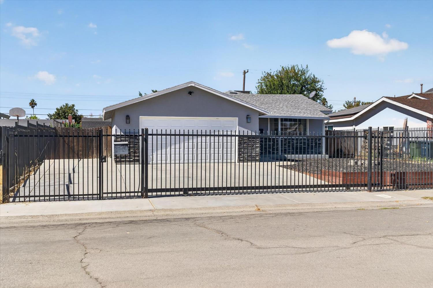Gray single-story home with a double garage, enclosed by a tall black metal fence.