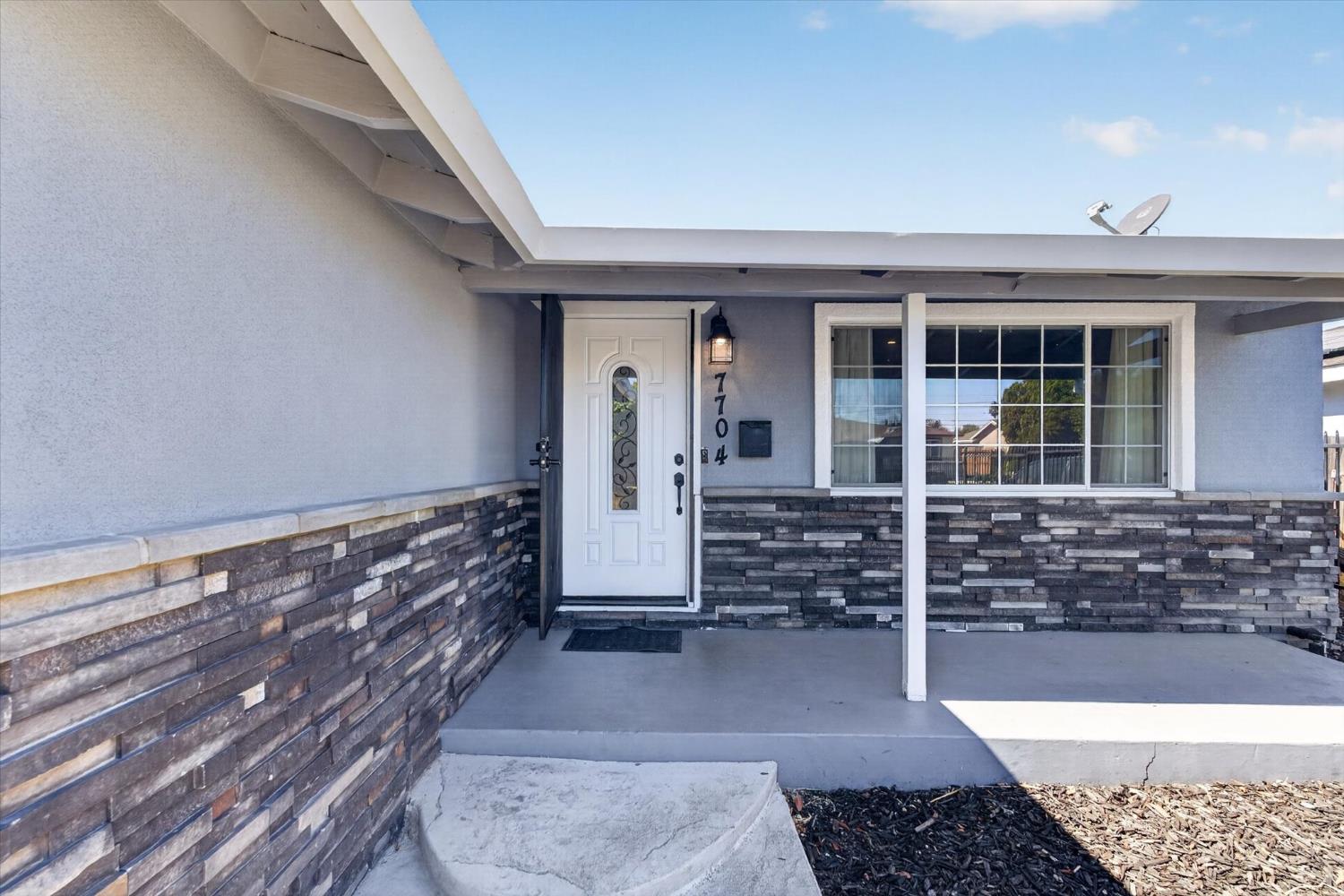 Home entrance with a covered porch, white door, and dark stacked-stone exterior.