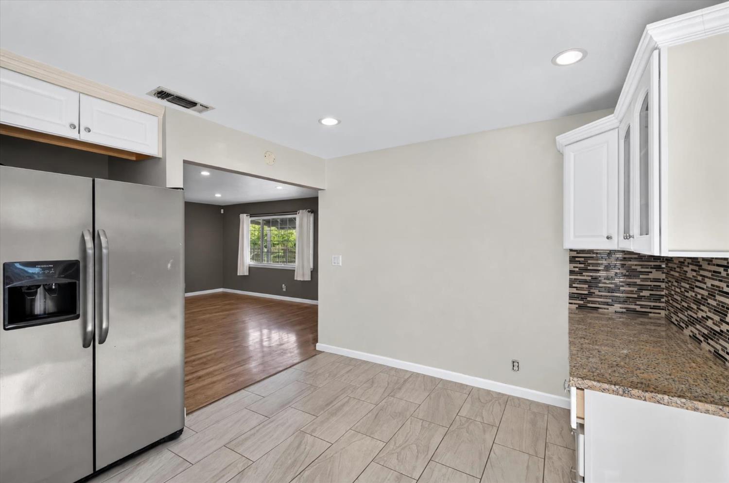 Kitchen with stainless steel refrigerator, mosaic backsplash, and an open doorway to the living area.