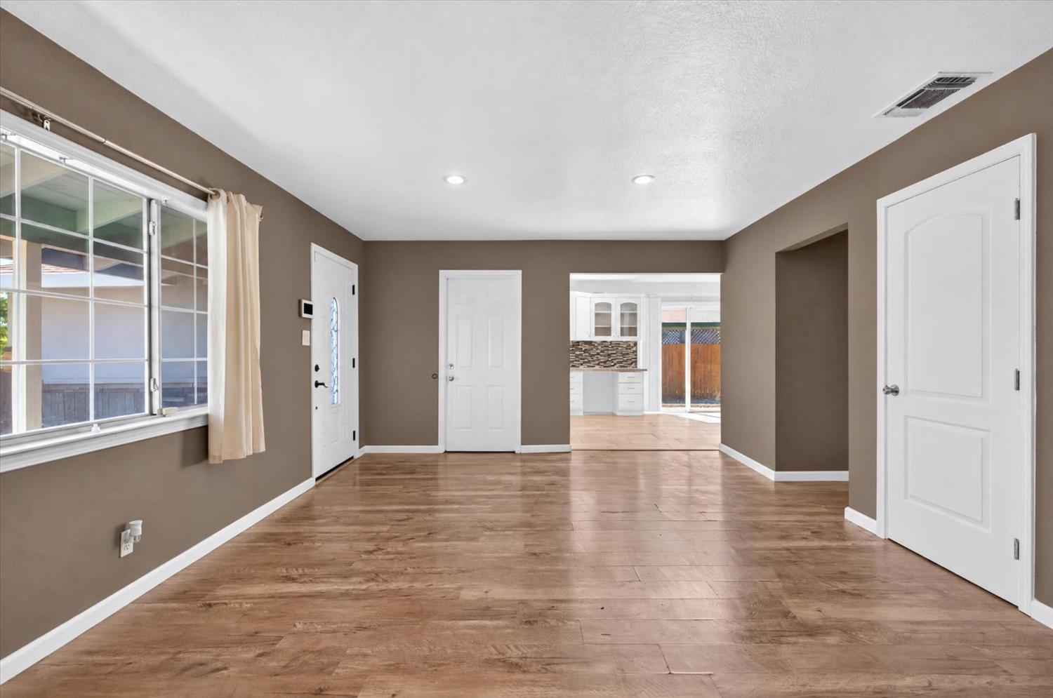 Vacant living room with wood-look flooring and a view into the kitchen.