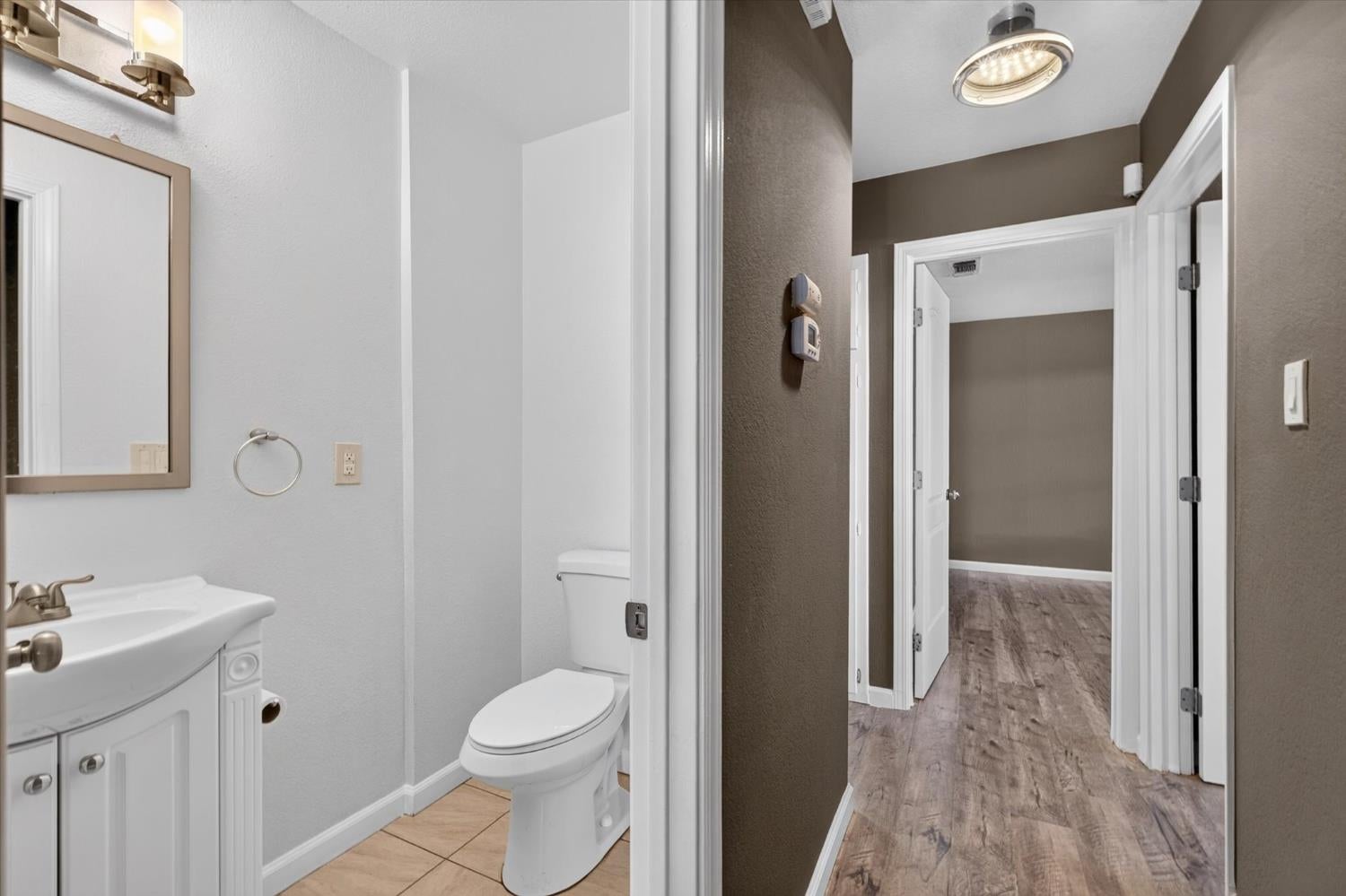 Bathroom with a white vanity and toilet opening onto a wood-look floored hallway.