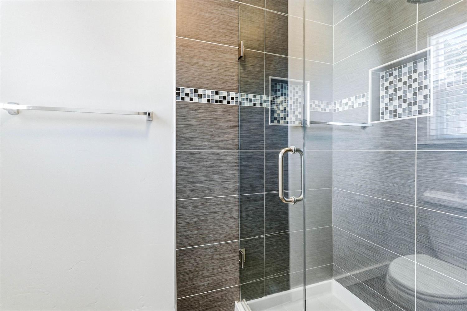 Bathroom shower with gray tile, mosaic accents, and a clear glass enclosure.