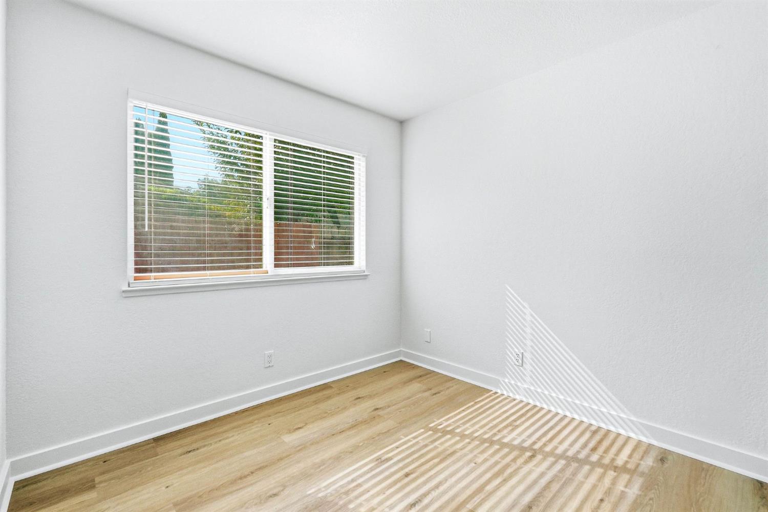 Empty room with light wood floors and sunlight casting striped shadows through window blinds.