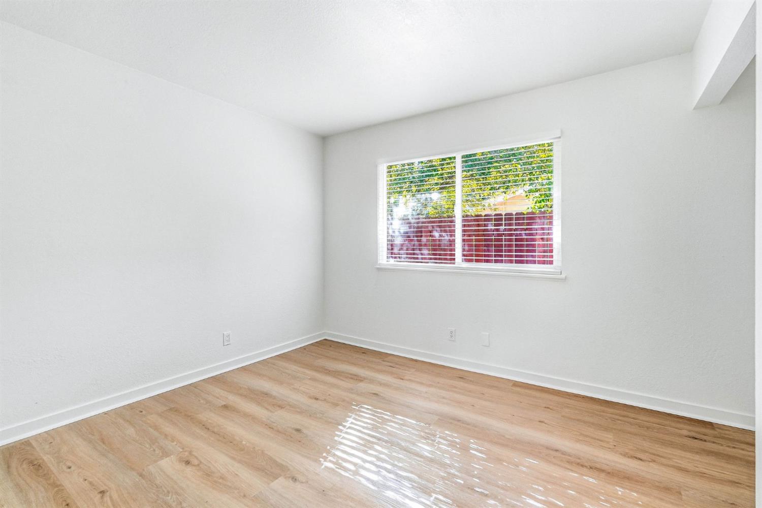 Empty room with light wood floors and a window overlooking trees and a red fence.
