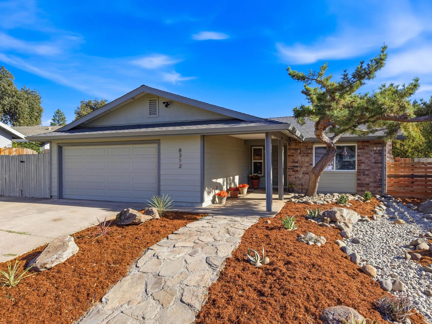 Single-story home with a two-car garage, stone walkway, and landscaped front yard.