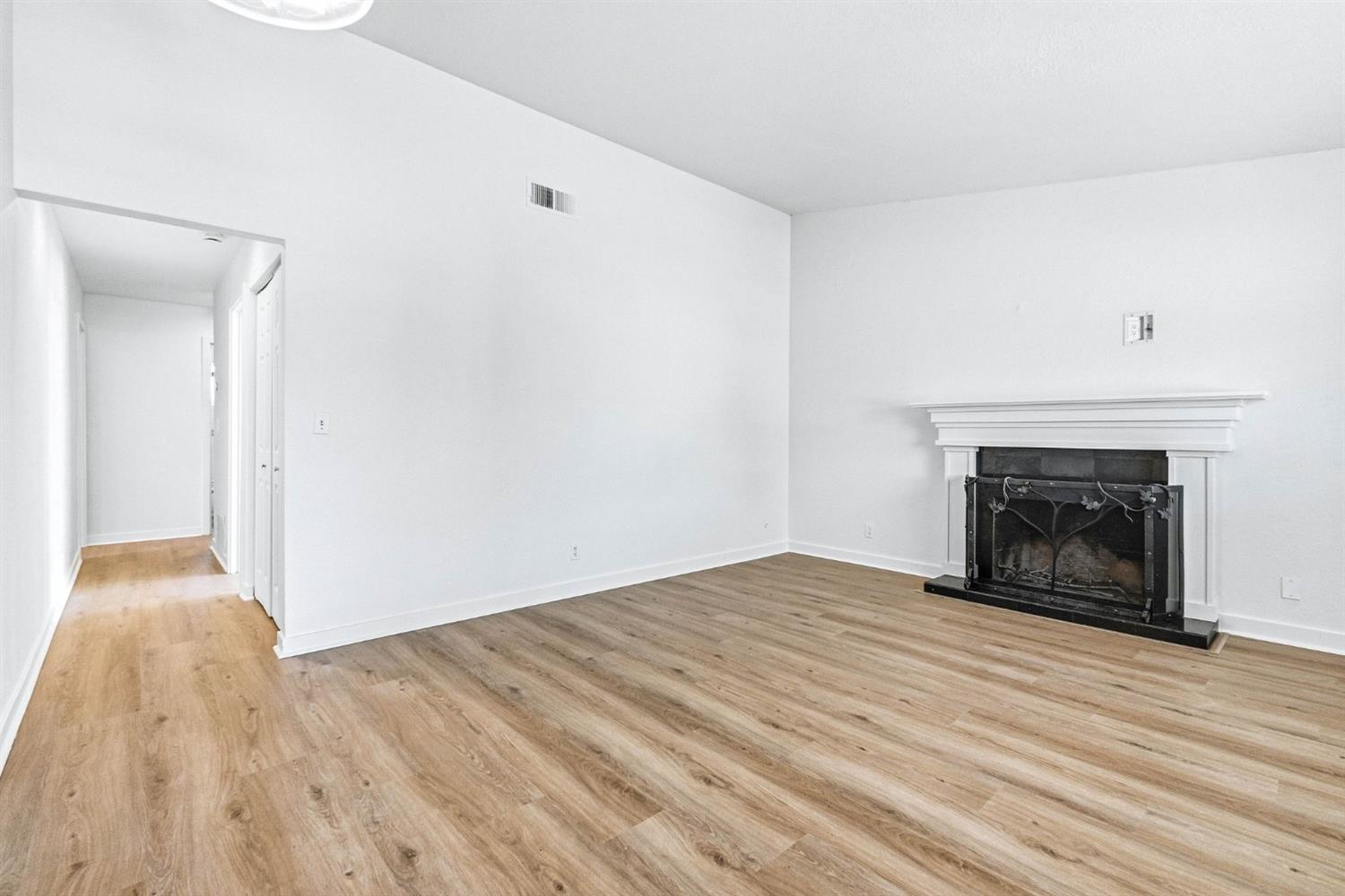 Vacant living room with wood-look floors and a white fireplace with a dark metal screen.