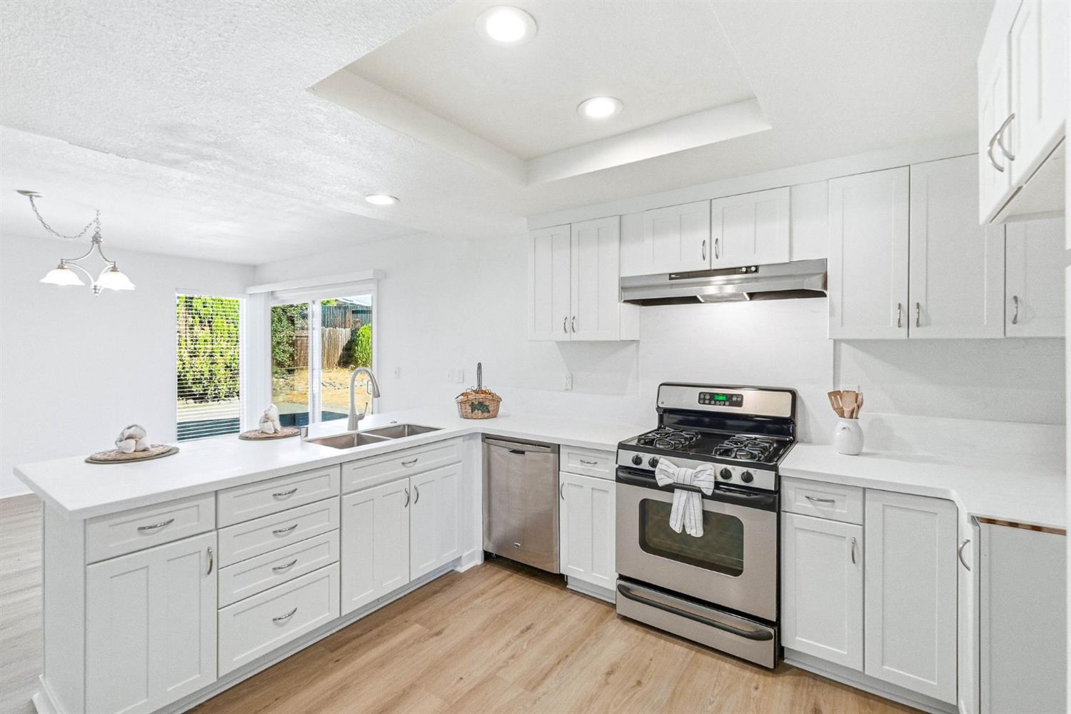 Renovated white kitchen with stainless steel appliances, a double-basin sink, and sliding glass doors.