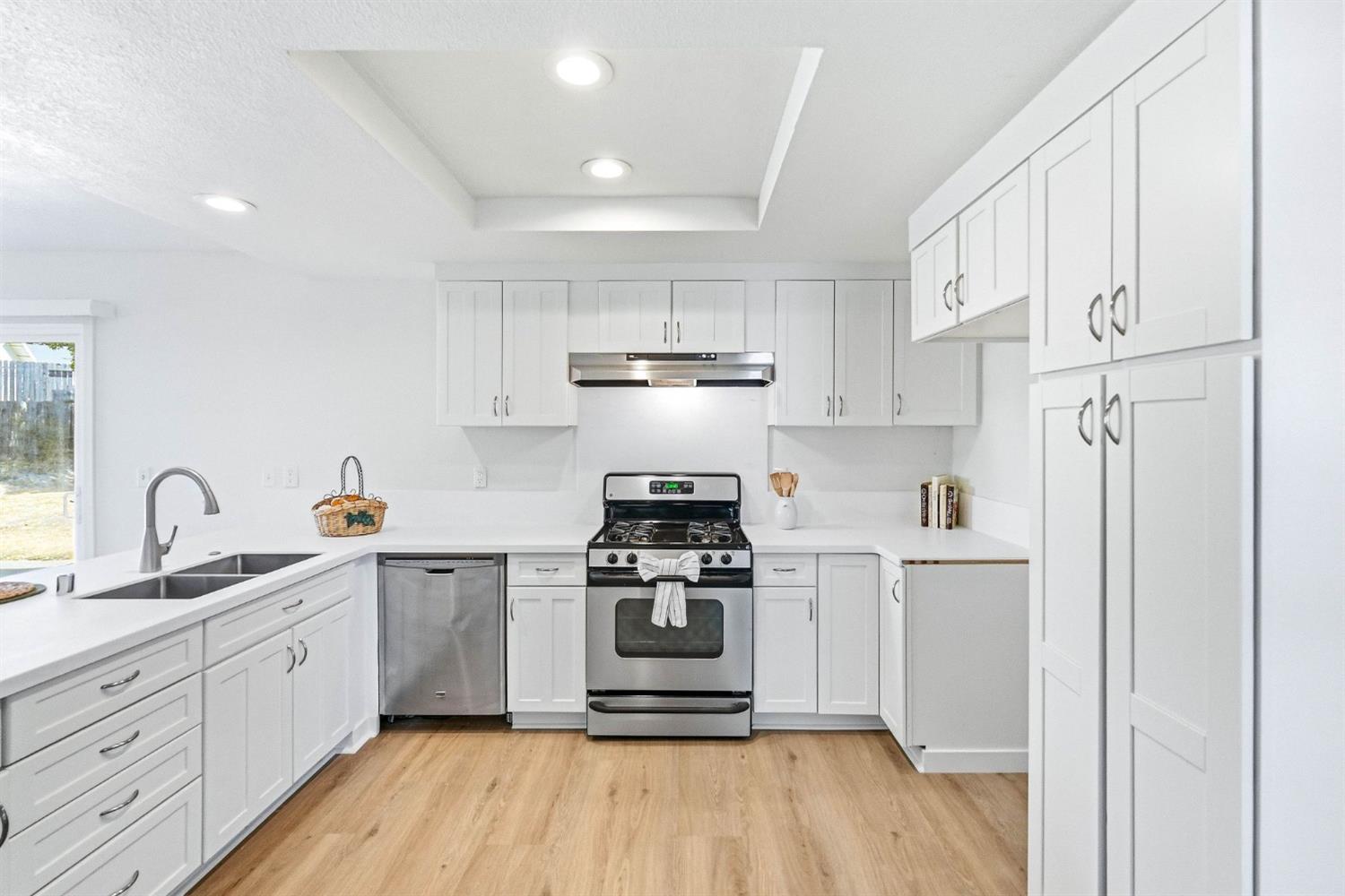 White kitchen with stainless steel appliances, shaker cabinets, and light wood flooring.
