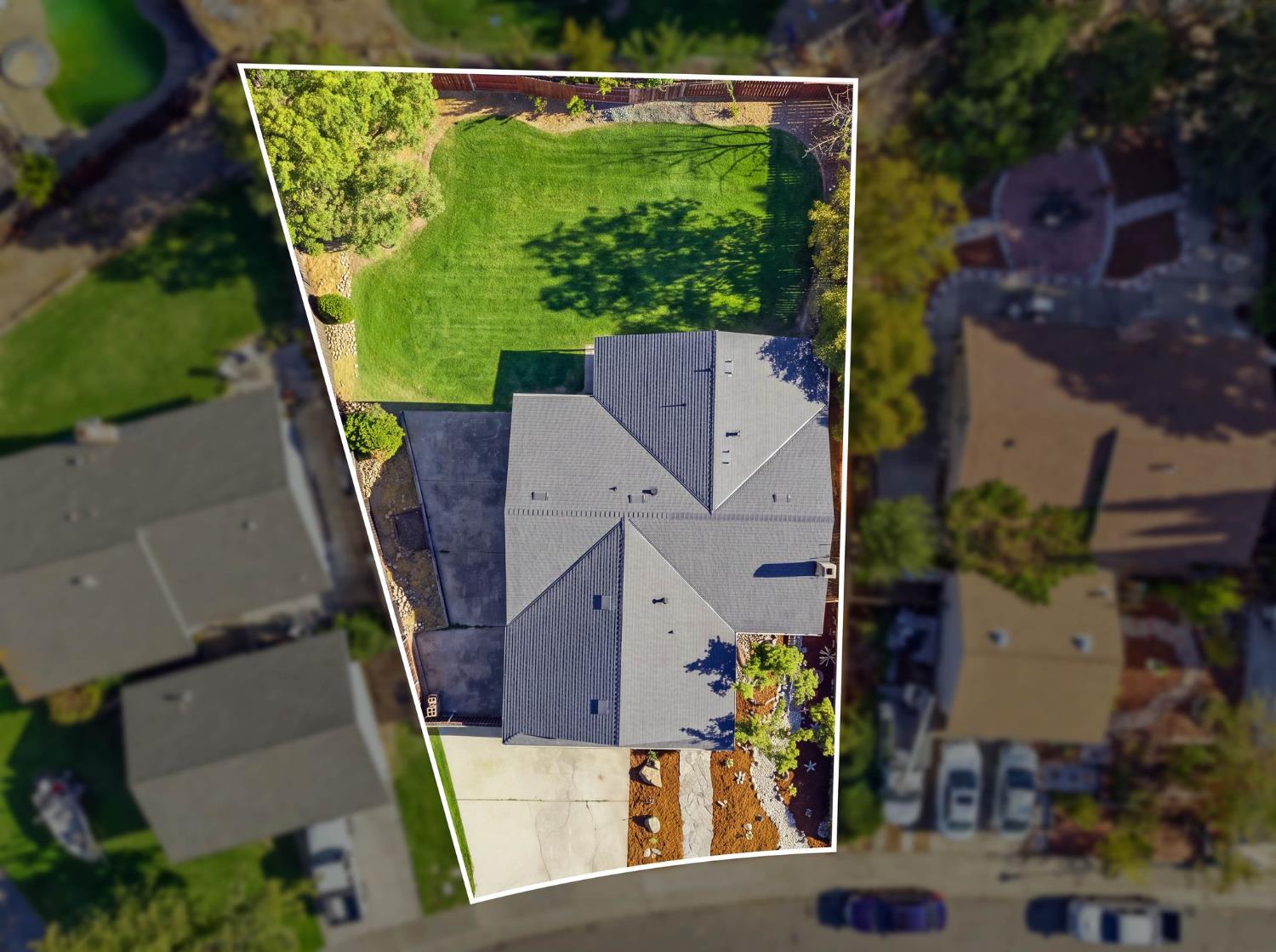 Aerial view of a home with a large fenced lawn, driveway, and landscaped yard.