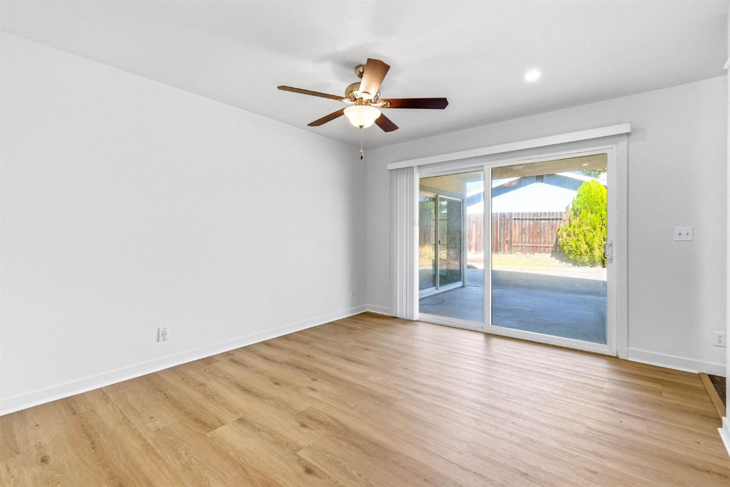 Vacant room with light wood flooring, a ceiling fan, and sliding glass doors to a patio.