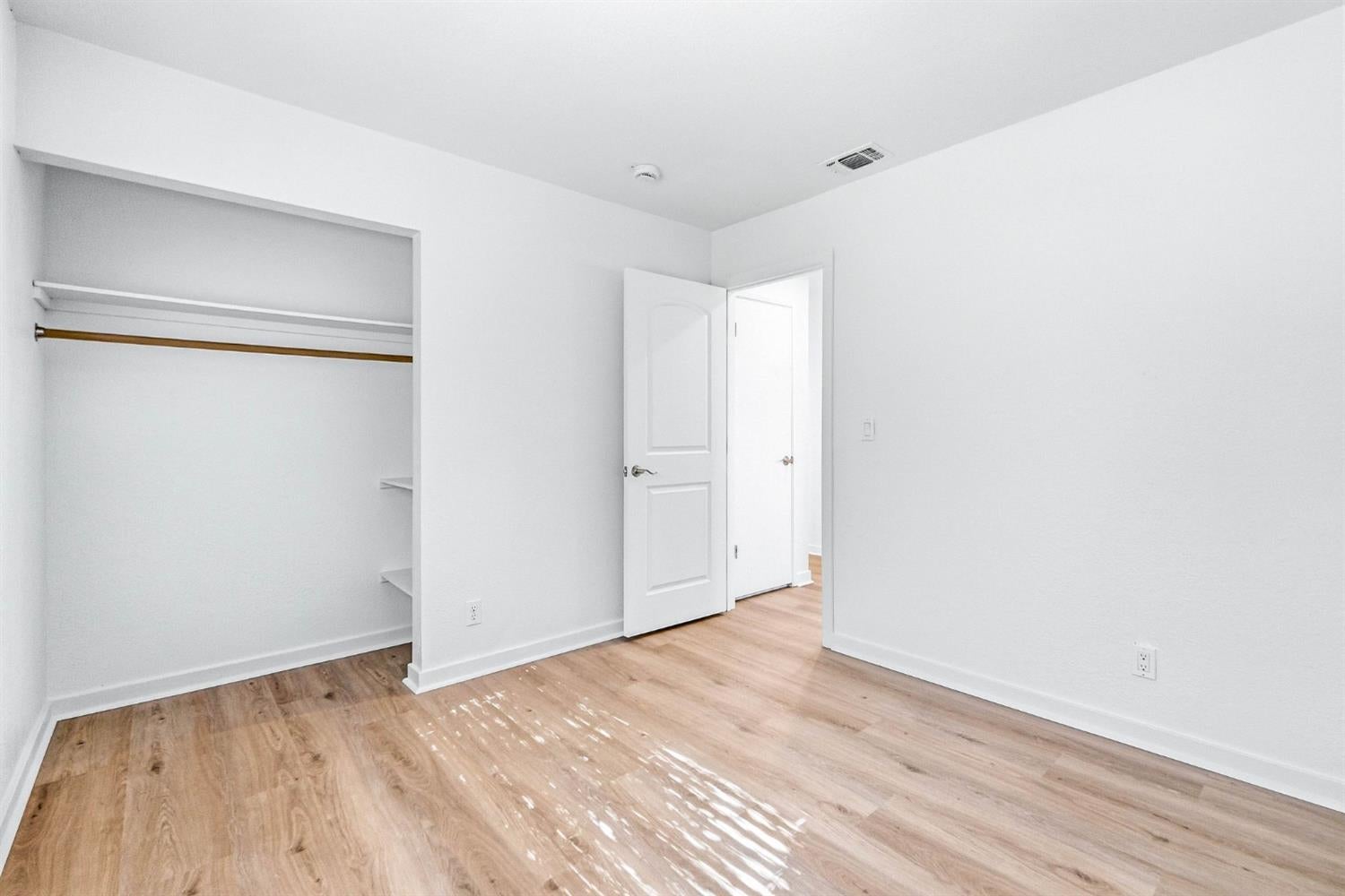 Empty bedroom with a large open closet and light wood-look flooring.