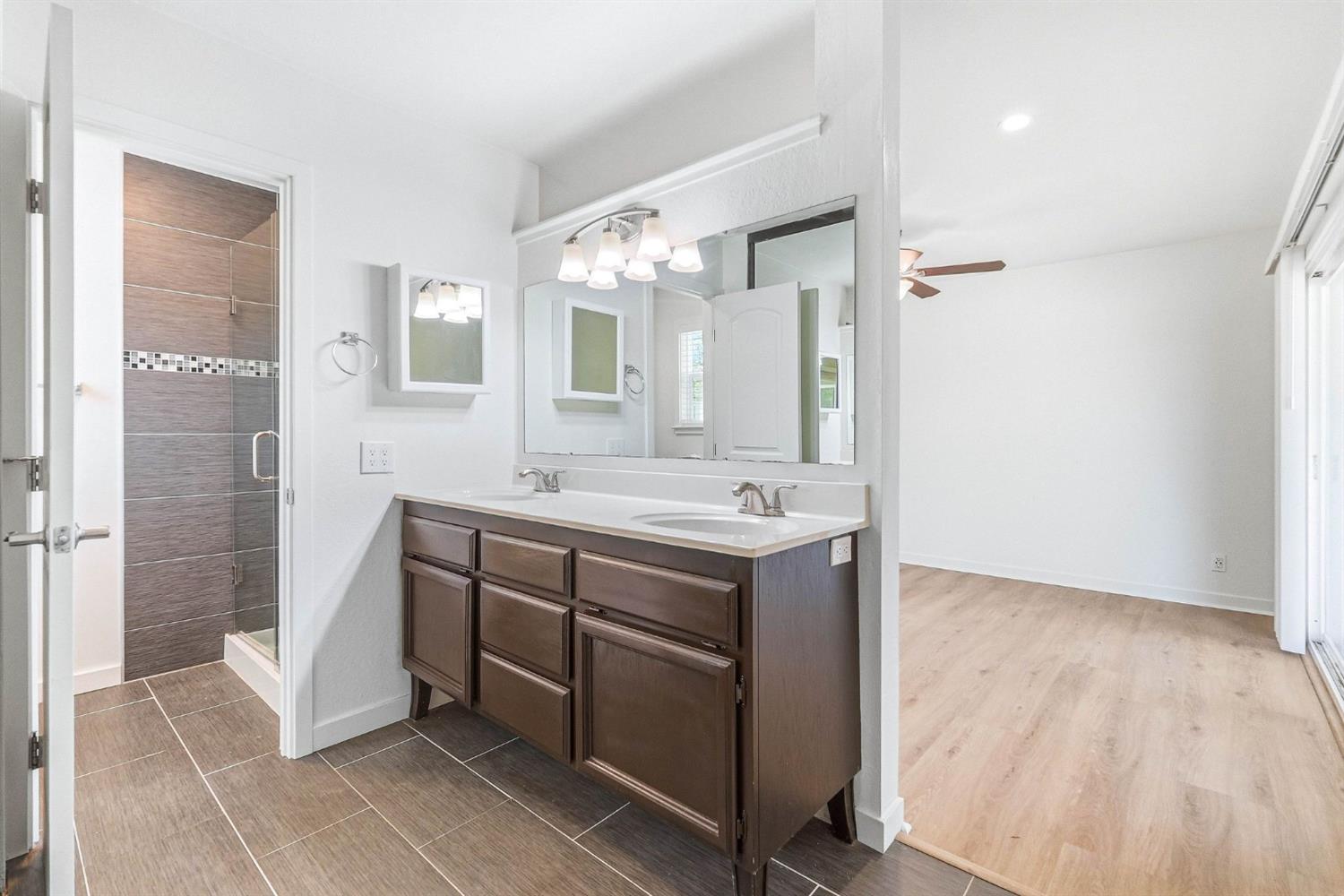 Bathroom with a dark double vanity and tiled shower, opening onto an empty room.