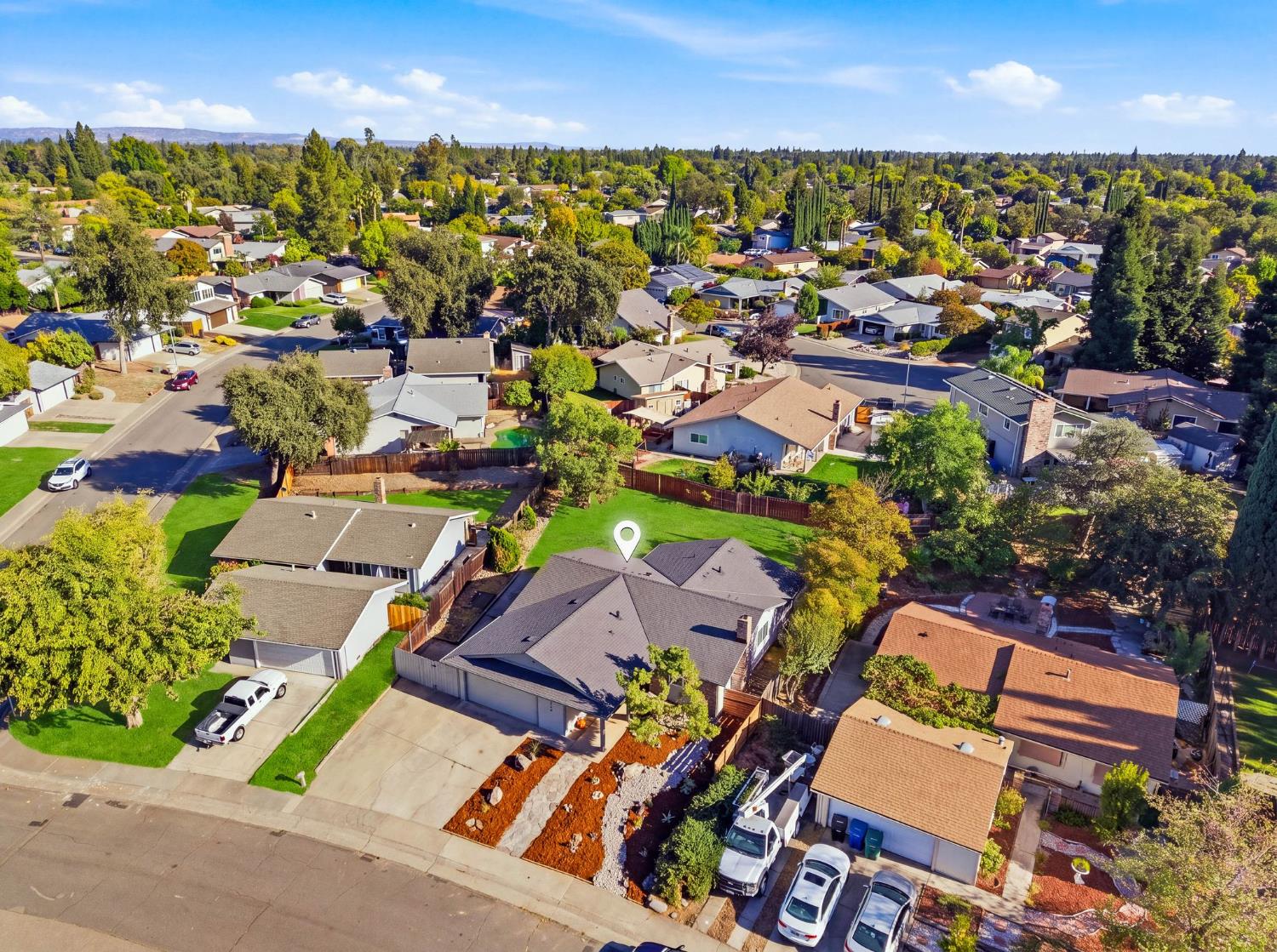Aerial neighborhood view with a map pin marking a single-story home among tree-lined streets.