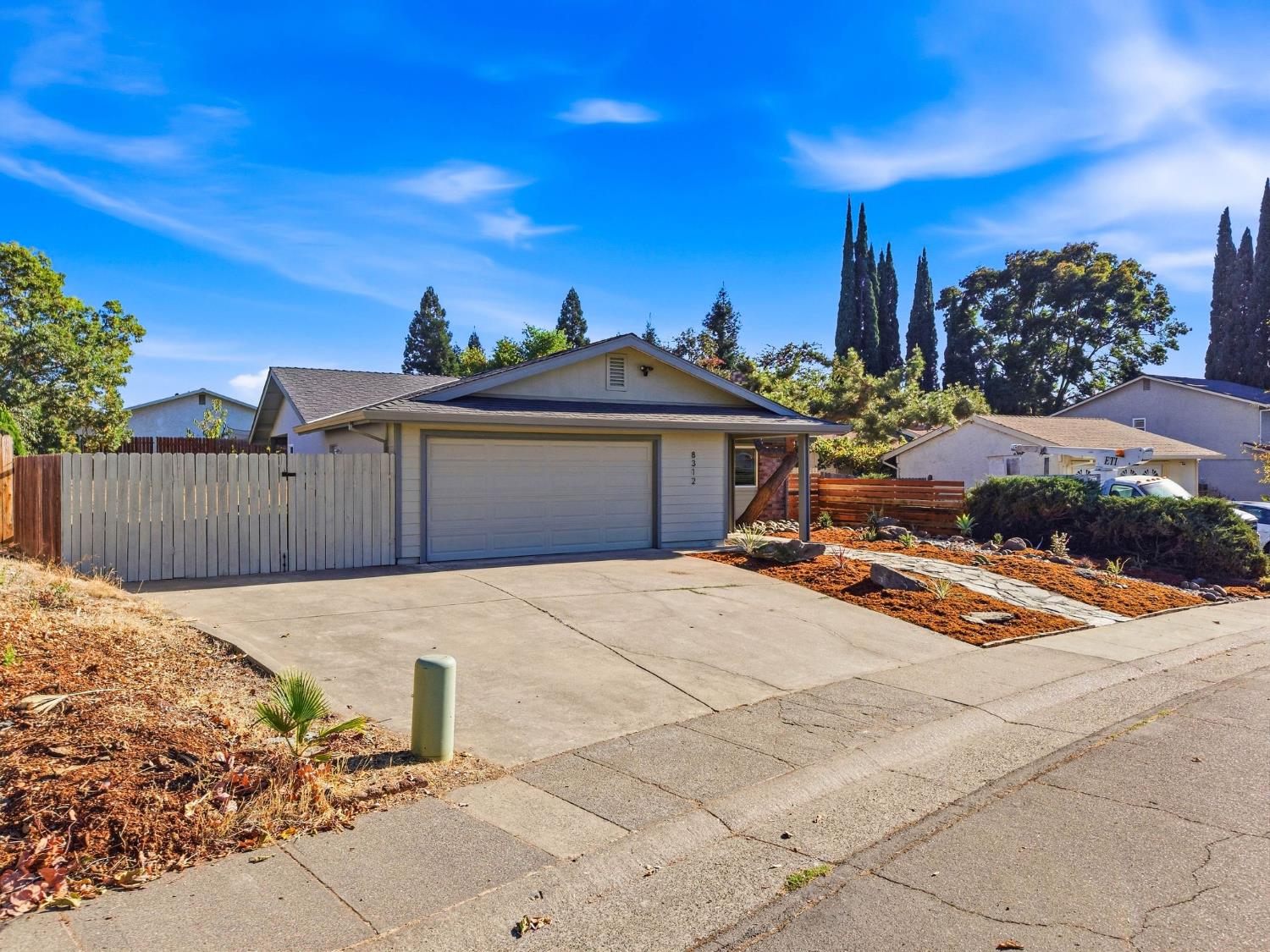 Single-story home with a broad garage, wide driveway, white fence, and landscaped front yard.
