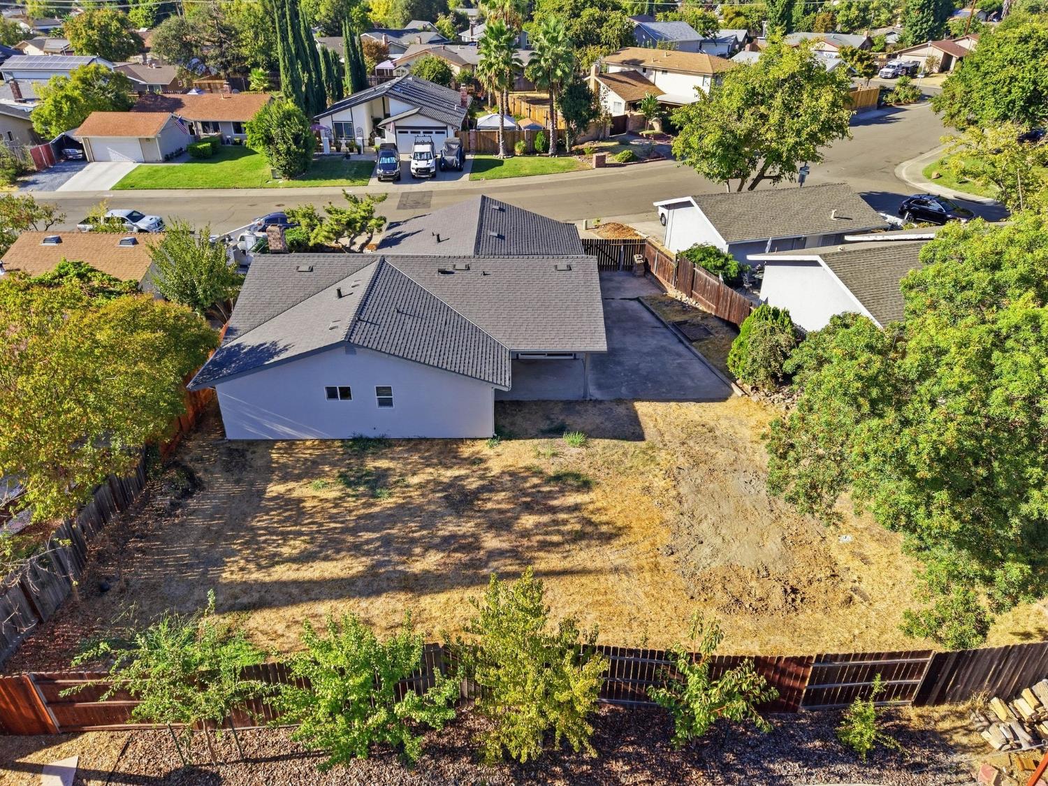 Aerial view of a single-story home, driveway, and large fenced backyard.