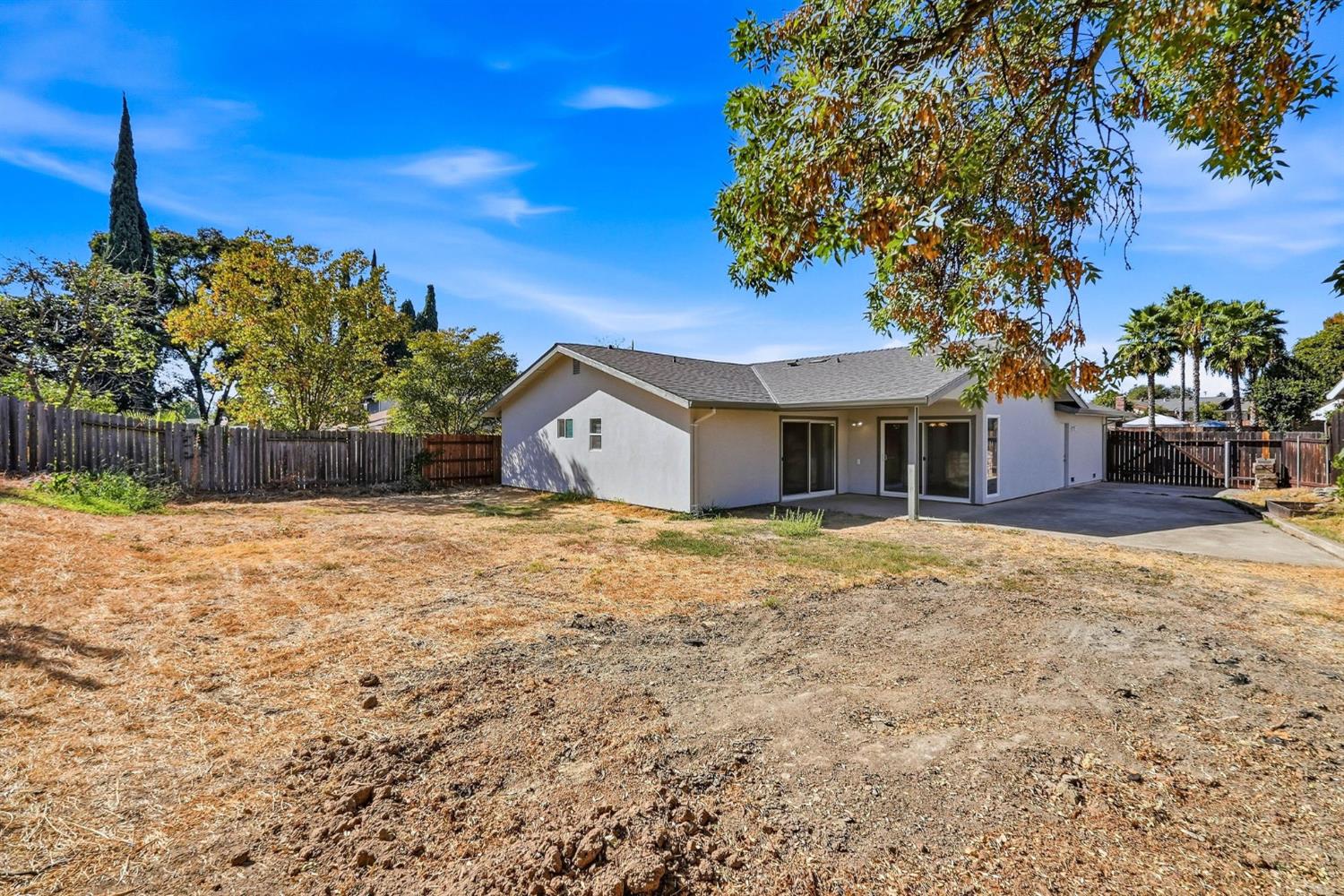 Rear of a single-story home with a covered patio overlooking a large dry, fenced backyard.